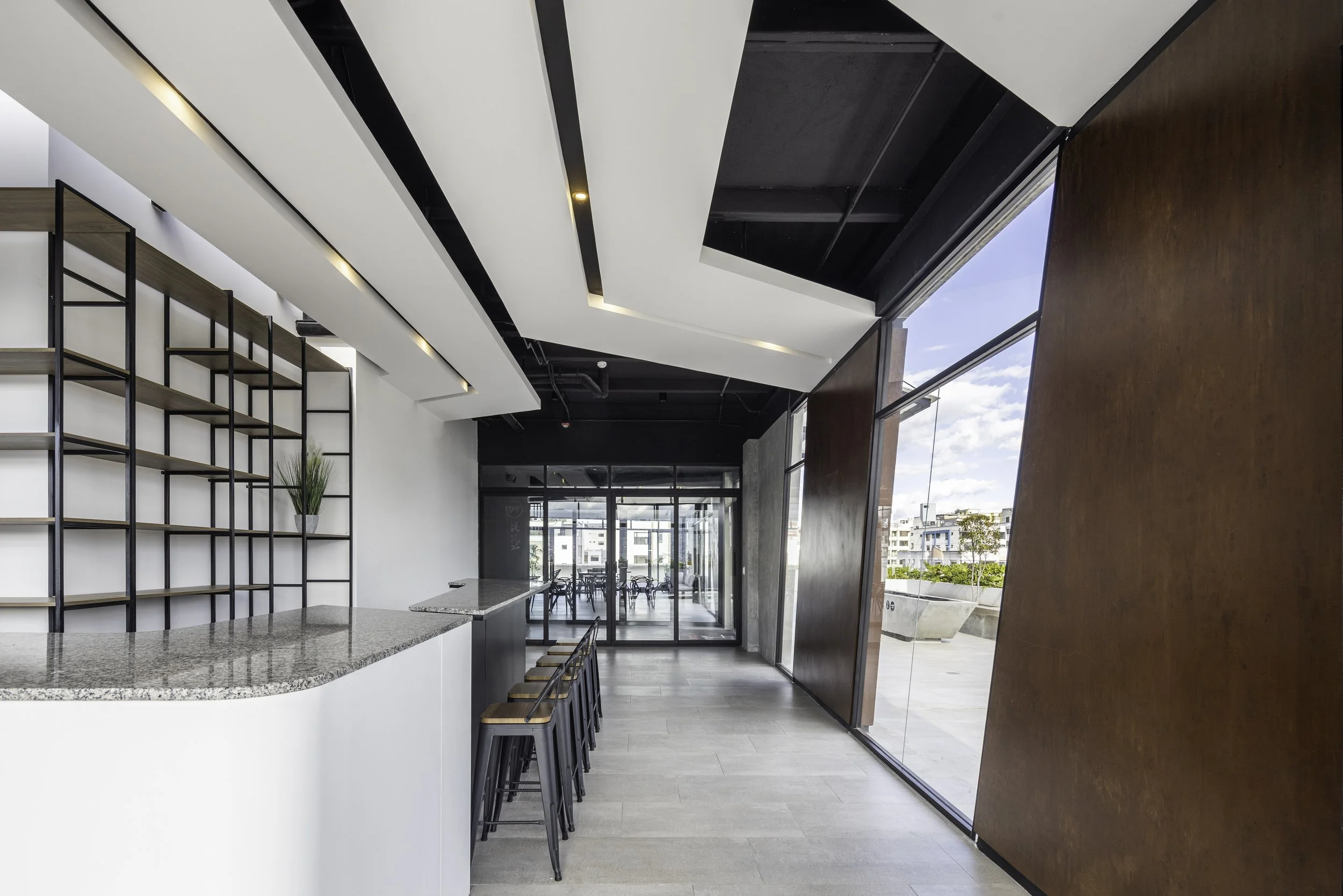 Interior moderno de un espacio con pared de madera, ventanas grandes, una barra de granito y estantes de metal en la pared izquierda.