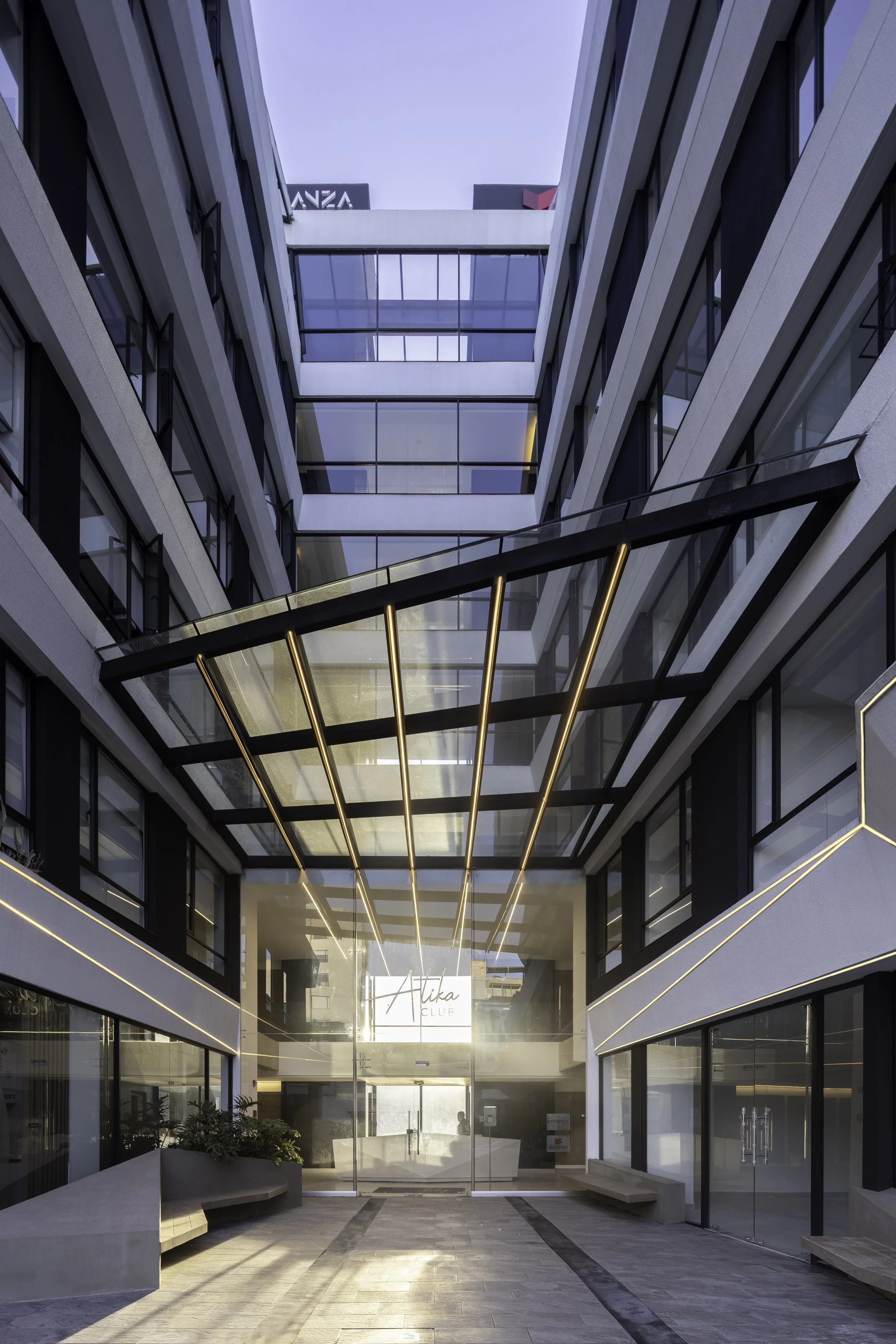 Vista del patio interior de un edificio moderno con cristaleras y balcones, con un letrero que dice "Aika Club" en la entrada.