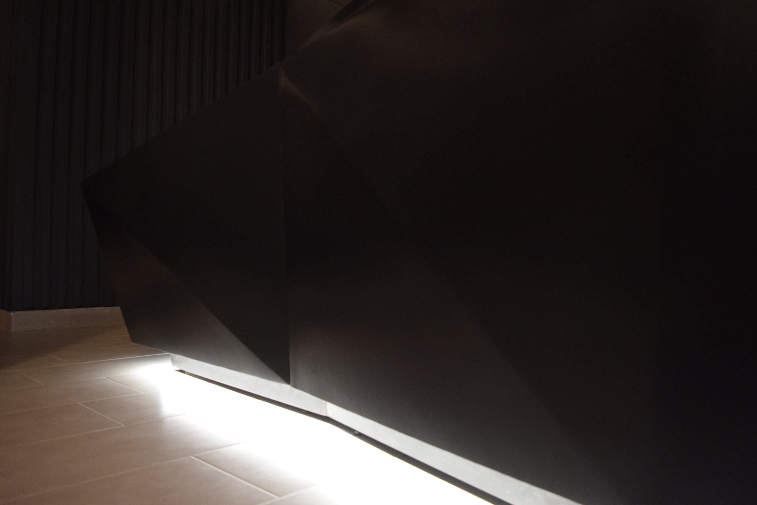 Mueble oscuro con iluminación debajo en un piso de baldosas claras.