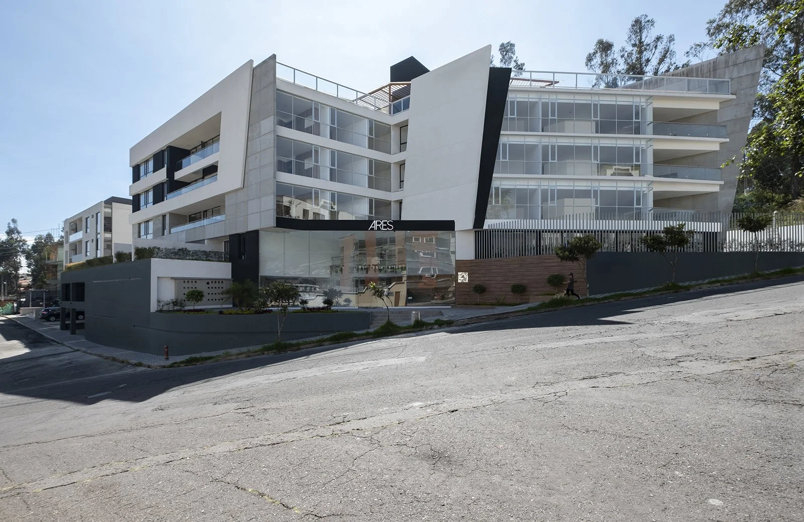 Edificio moderno de varios pisos con fachada de vidrio y líneas arquitectónicas angulares, frente a una calle en pendiente.