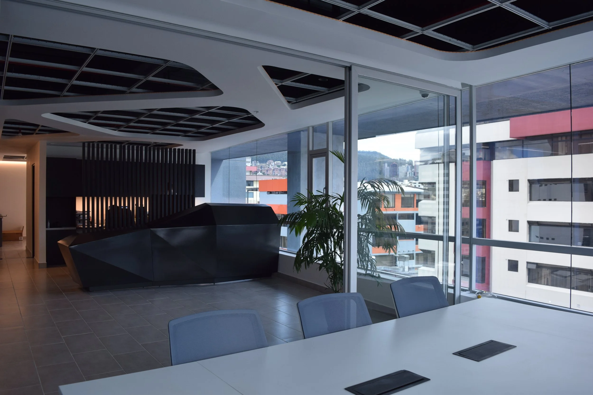 Oficina moderna con mesas, sillas y vista a edificios urbanos a través de ventana grande.