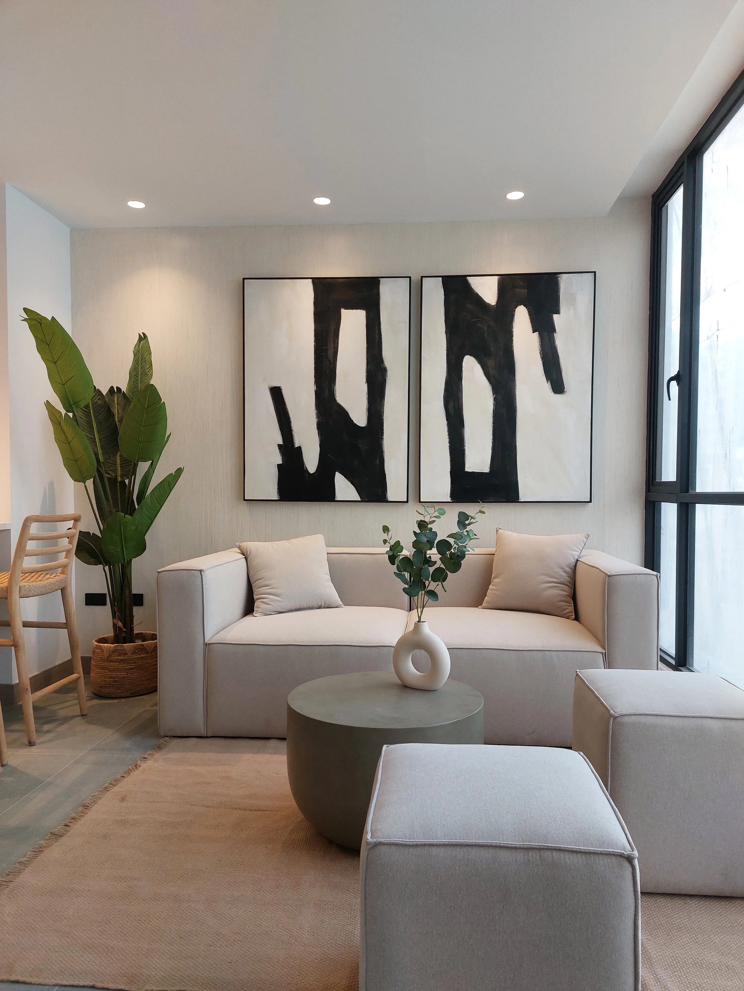 Sala moderna con sofá blanco, mesa de centro redonda, cuadros abstractos en la pared y plantas decorativas.