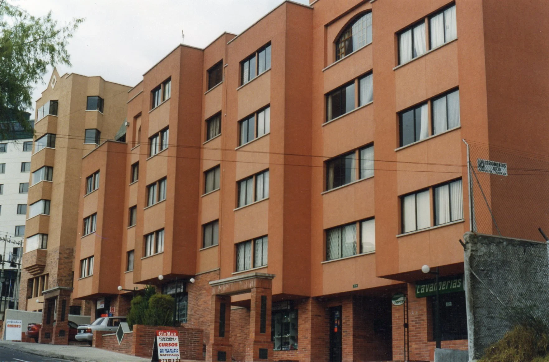 Edificio de departamentos de color marrón con varias ventanas y un acceso principal que tiene columnas de ladrillo a la entrada. Hay un letrero de un anuncio en la entrada del edificio.
