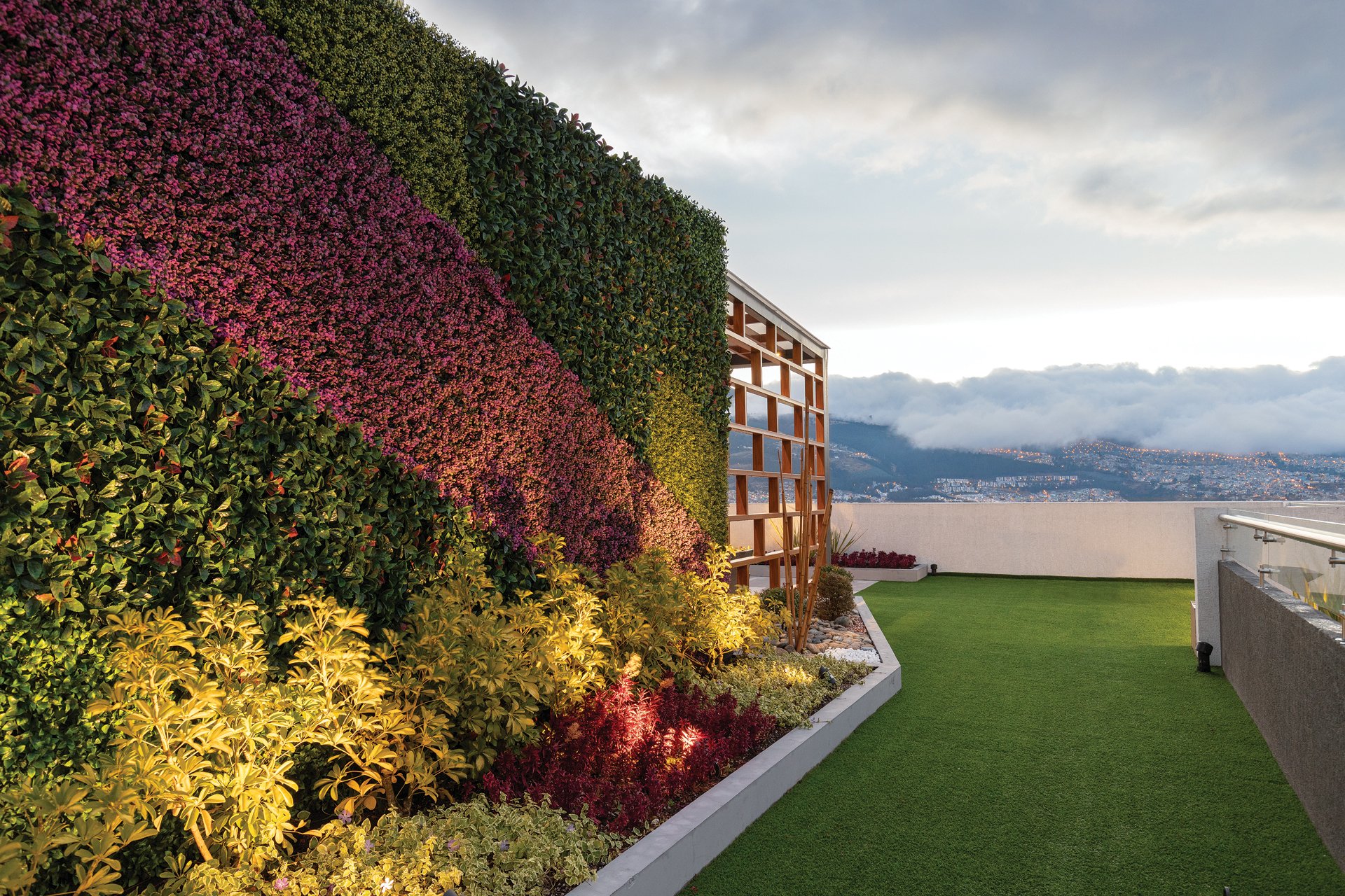 Jardín en la azotea con muro de plantas flores coloridas y vista de la ciudad y montañas.