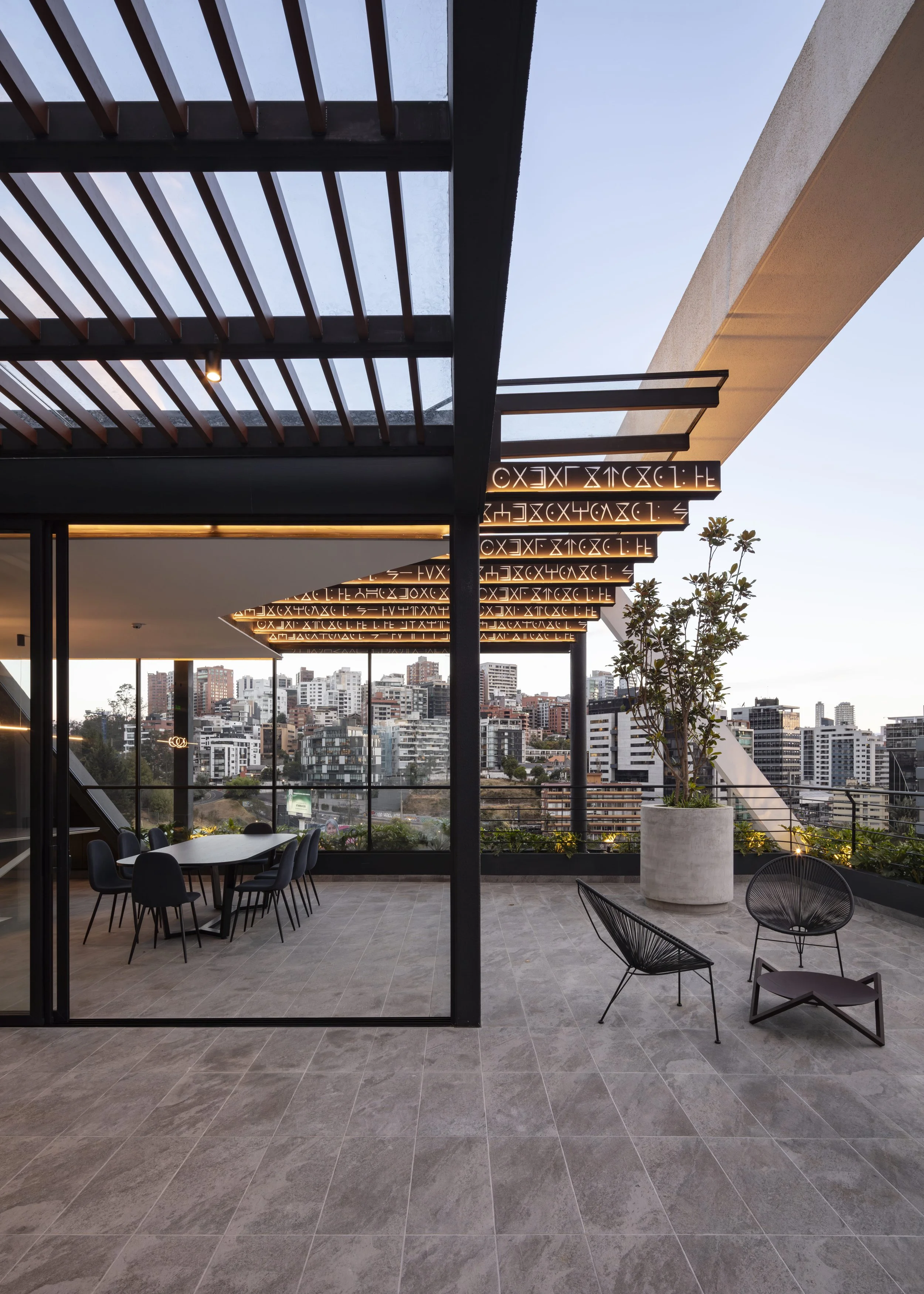 Quito vista de terraza de un edificio moderno con vista a la ciudad por sector el Batan, con mobiliario de comedor y plantas decorativas, estructura de techo con iluminación