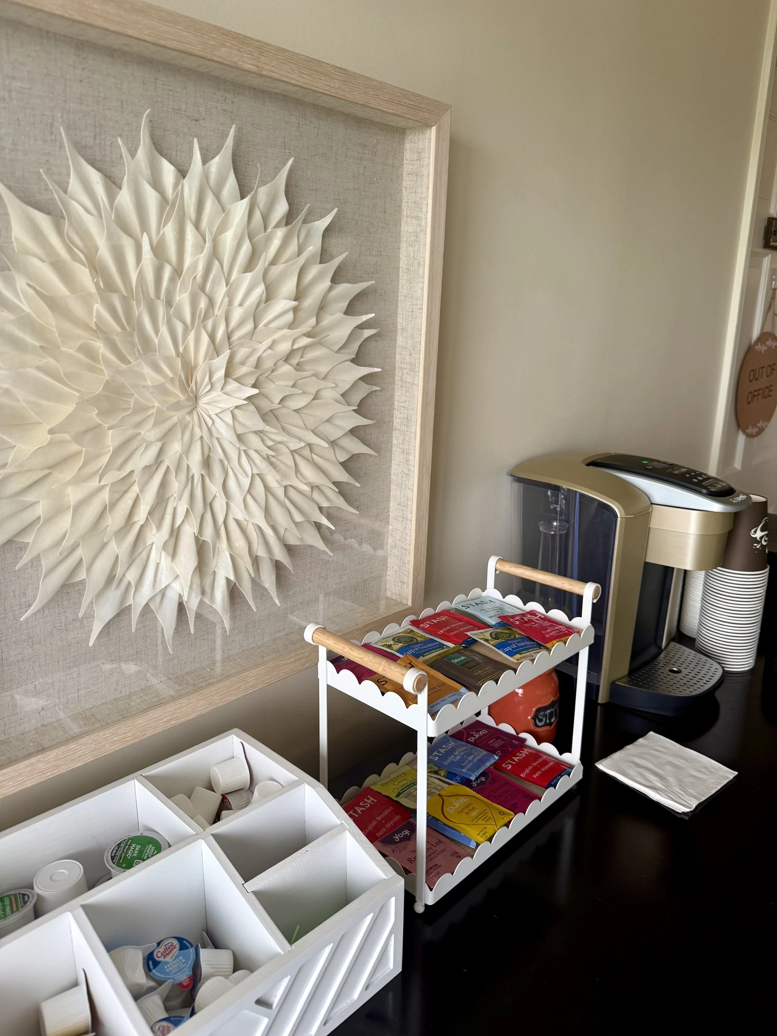 Arrangement of snacks and condiments on a countertop with a wall art piece depicting a white floral design in the background.