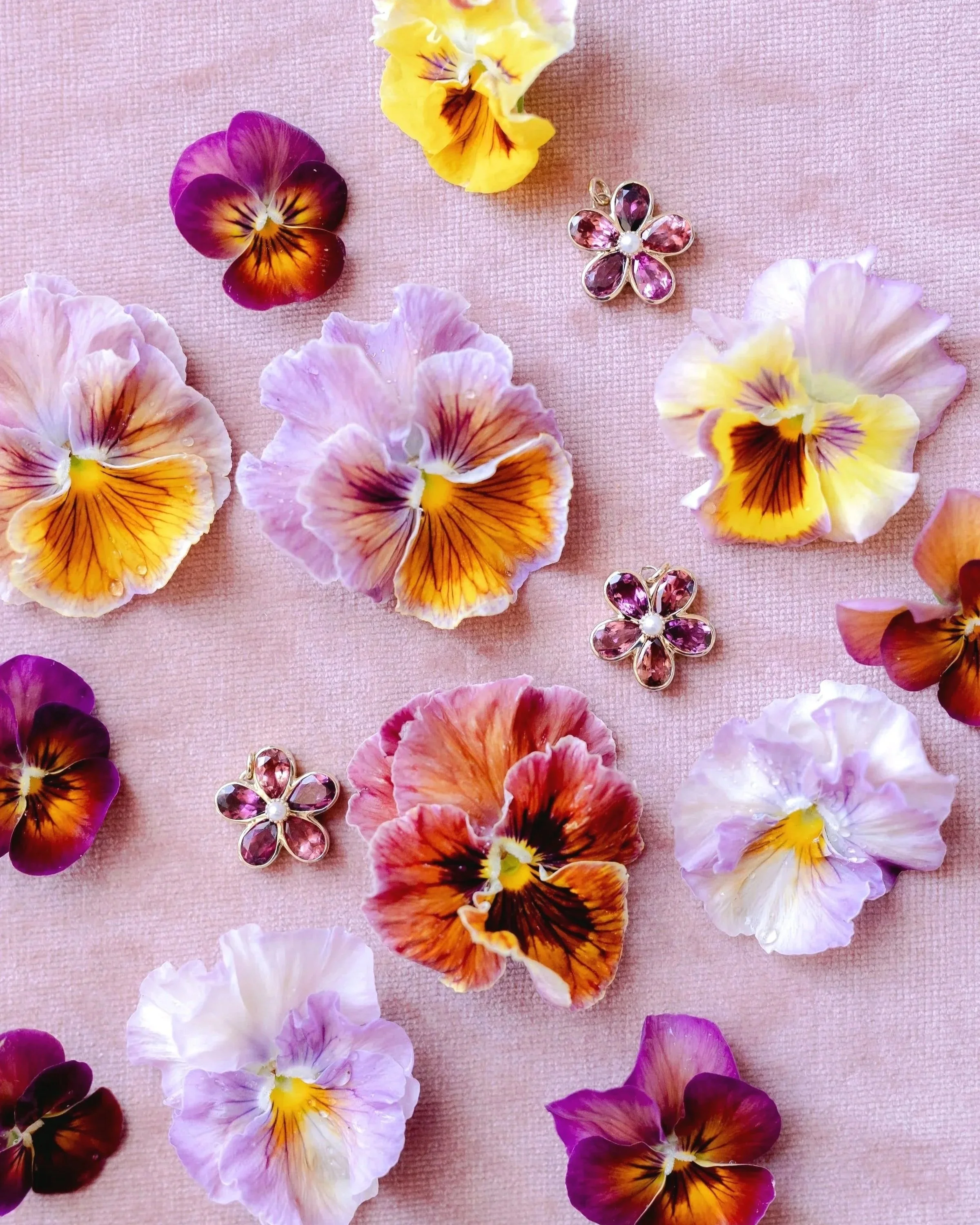 Colorful flowers and pink jewelry with pink gemstones arranged on a pink textured surface.