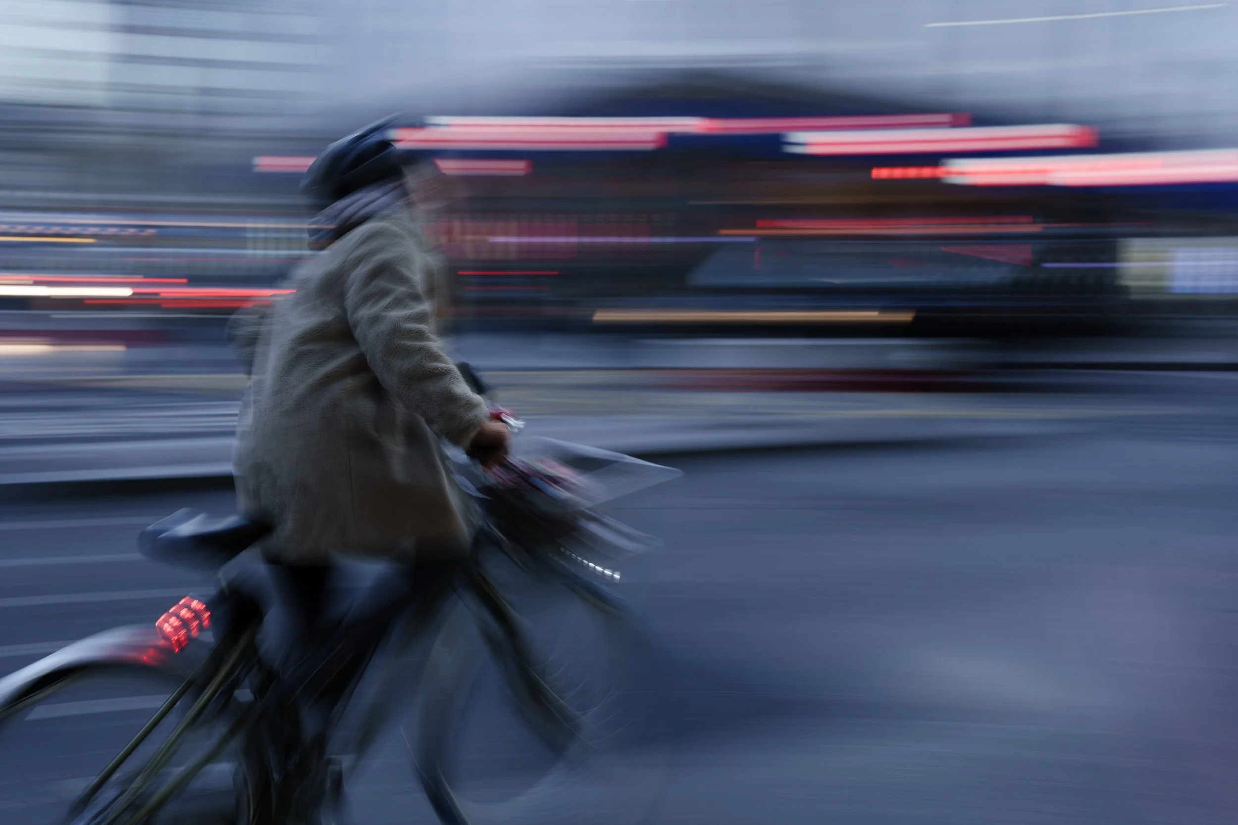 A person riding a bicycle on a city street during twilight with streaks of light indicating motion.