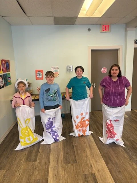 Four children standing indoors, each with a plastic bag decorated with a bunny design, participating in an Easter or spring activity.