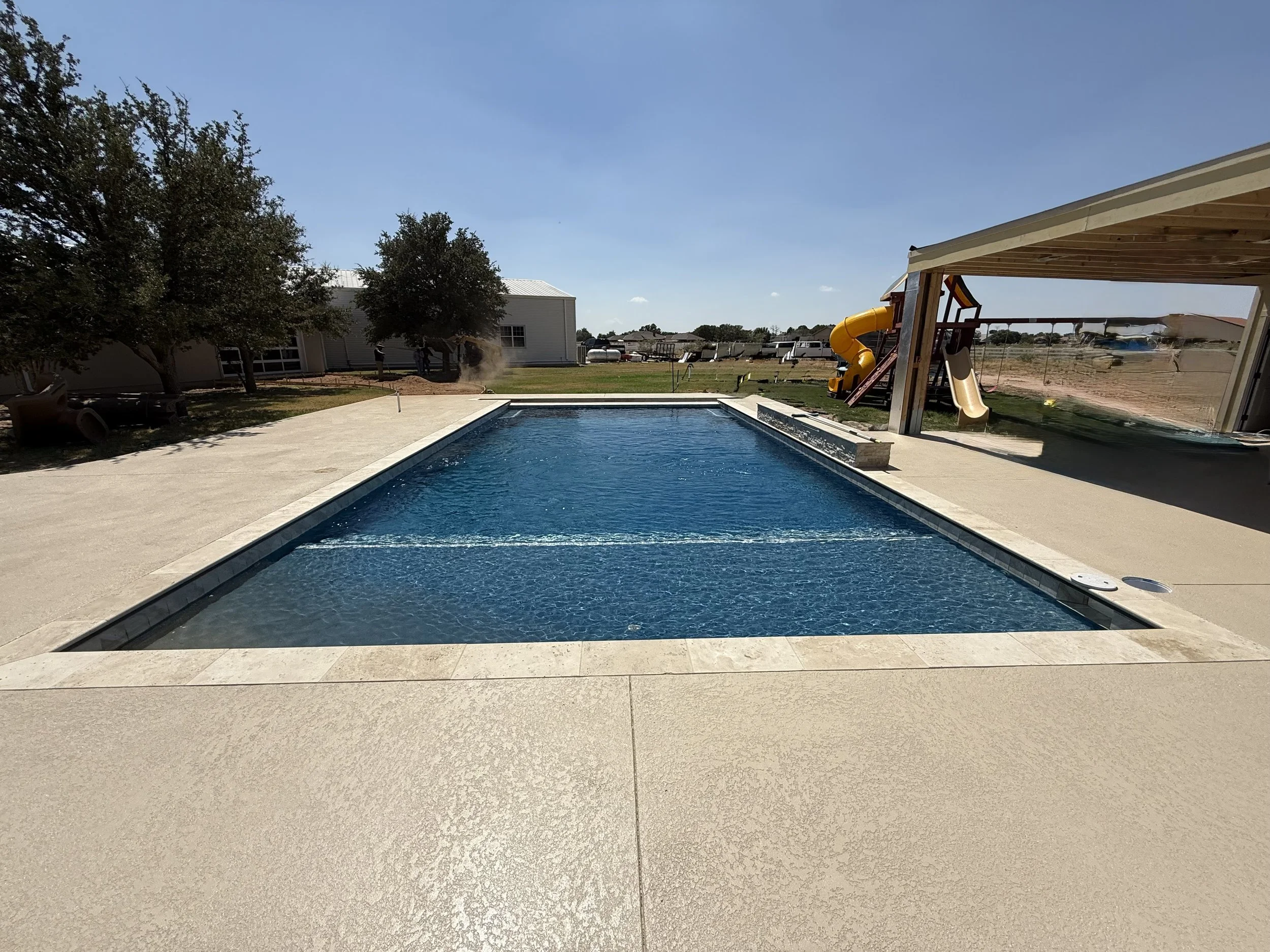 Clean backyard pool with playset in the background under clear Texas skies.