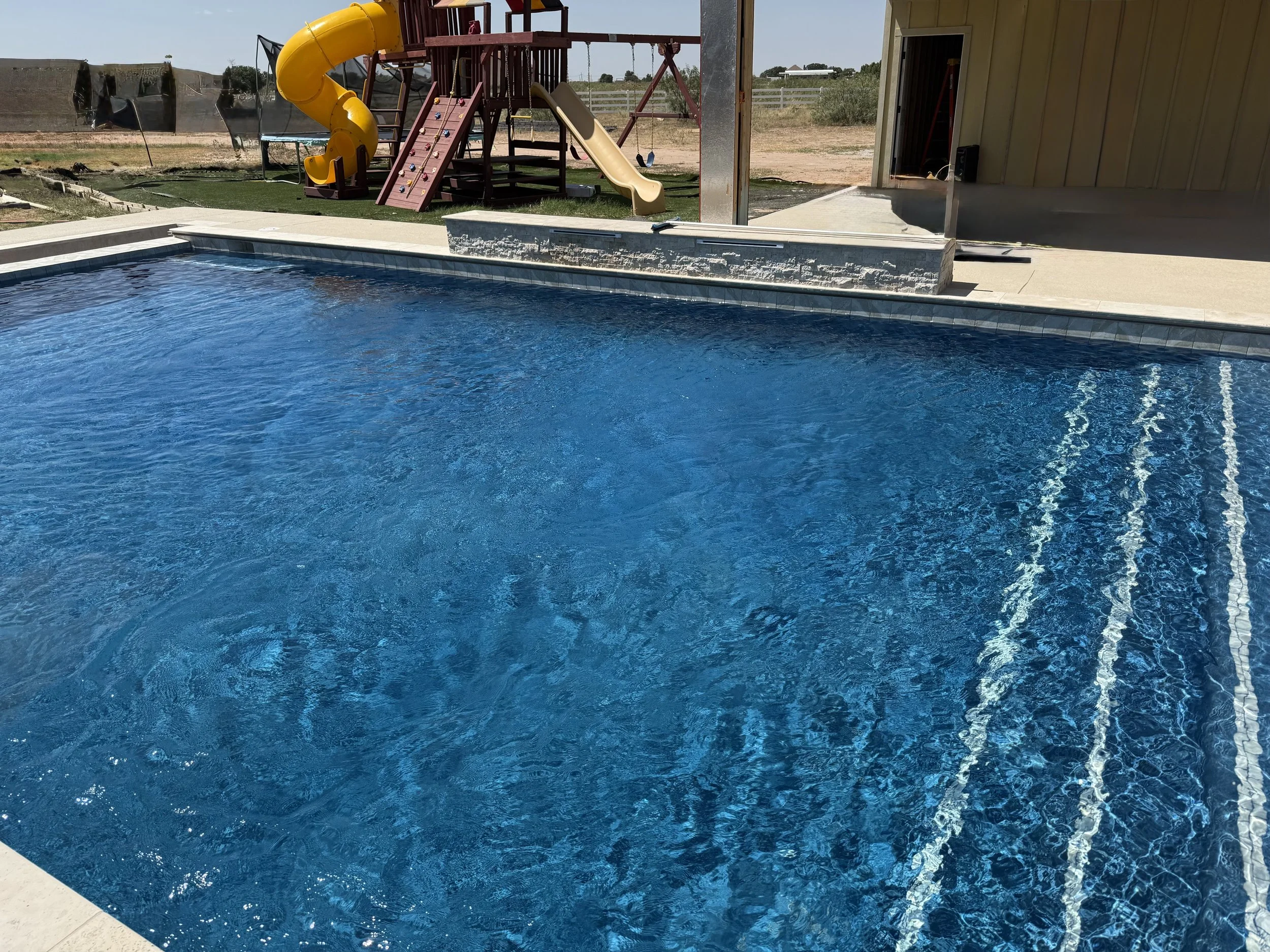 Large backyard pool with playset and clean water after maintenance.