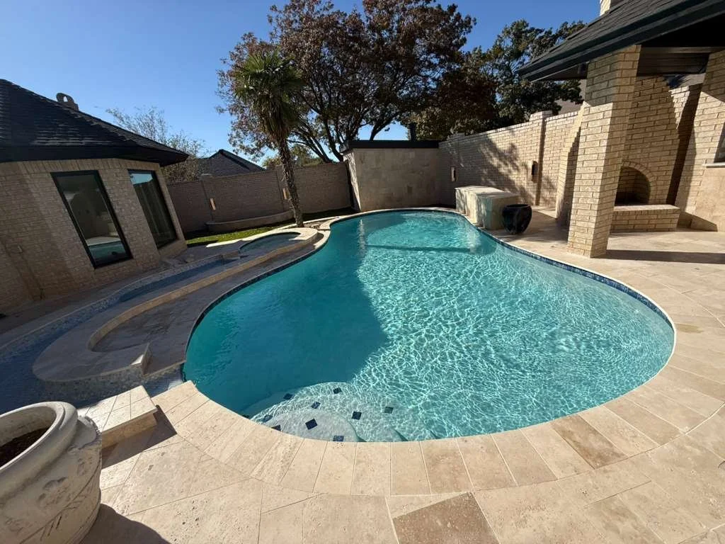 Bright blue freeform pool with spillover spa and surrounding landscaping.