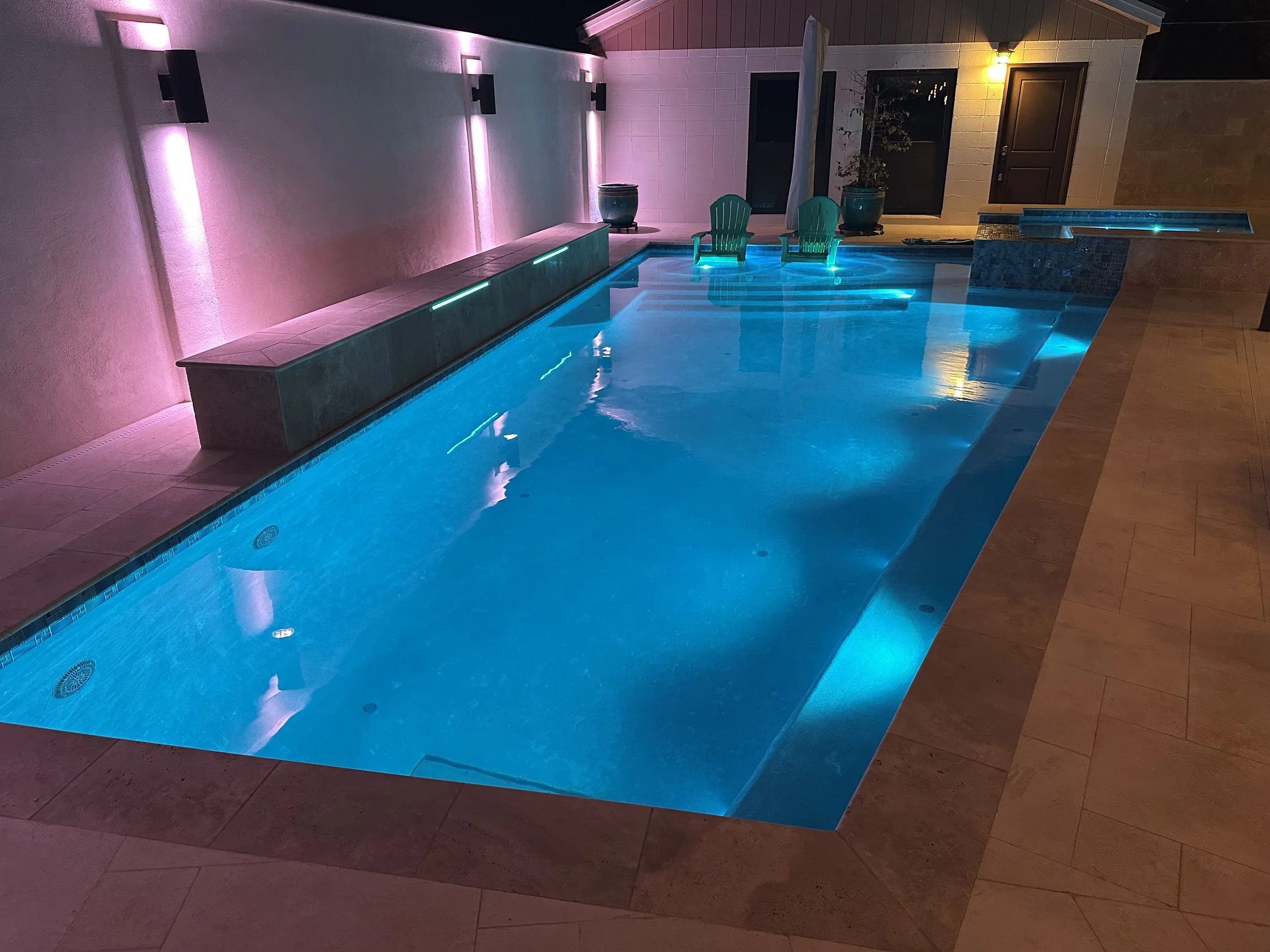 Residential pool glowing with aqua and magenta LED lighting.