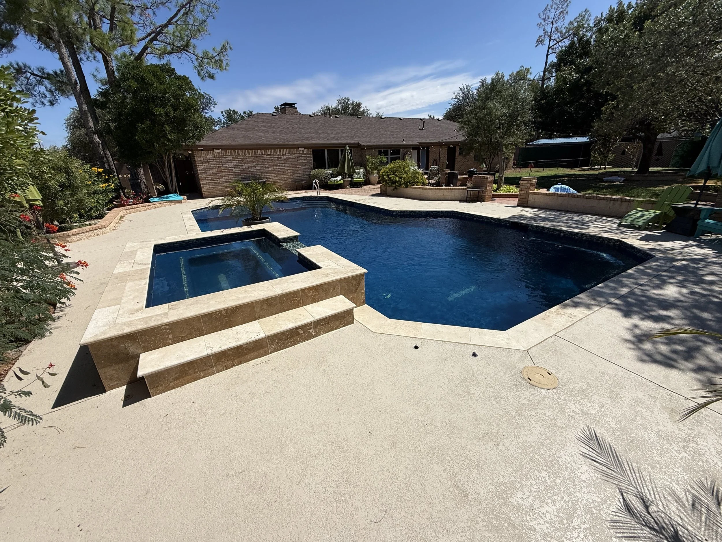 Backyard pool and attached spa surrounded by trees and patio area.
