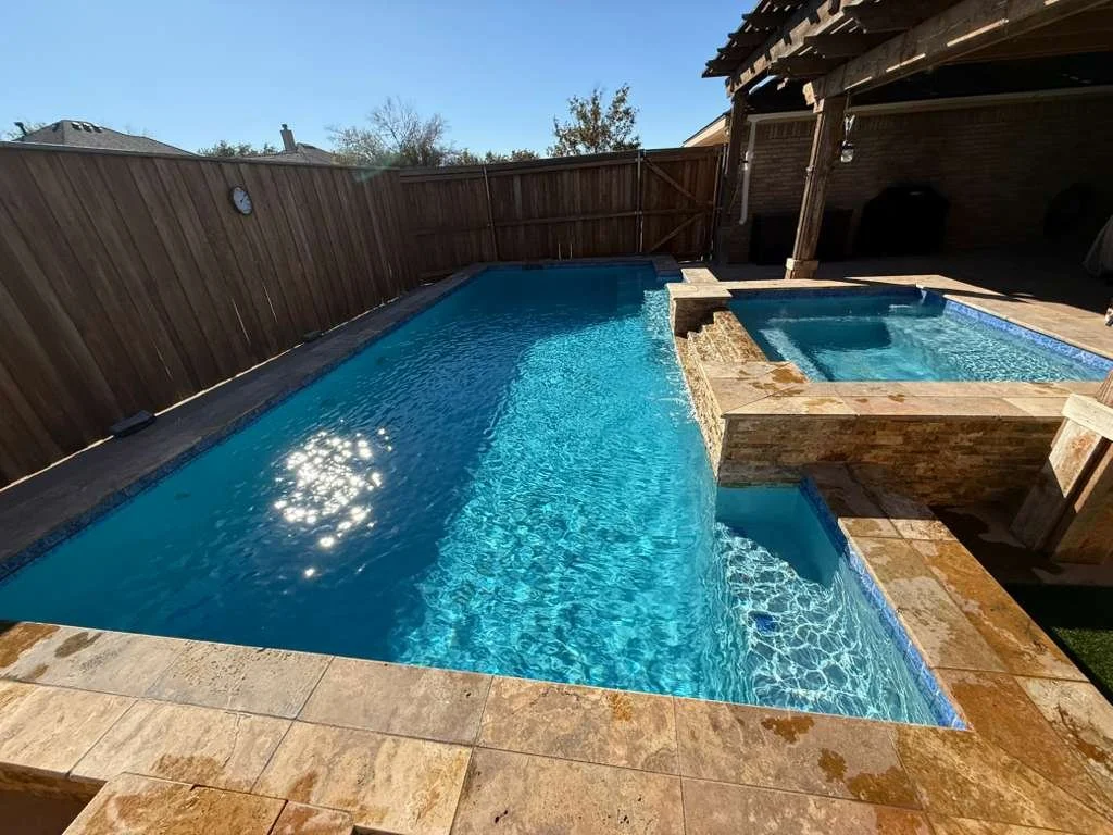 Clean modern backyard pool with raised stone spa and clear blue water in Midland, Texas.