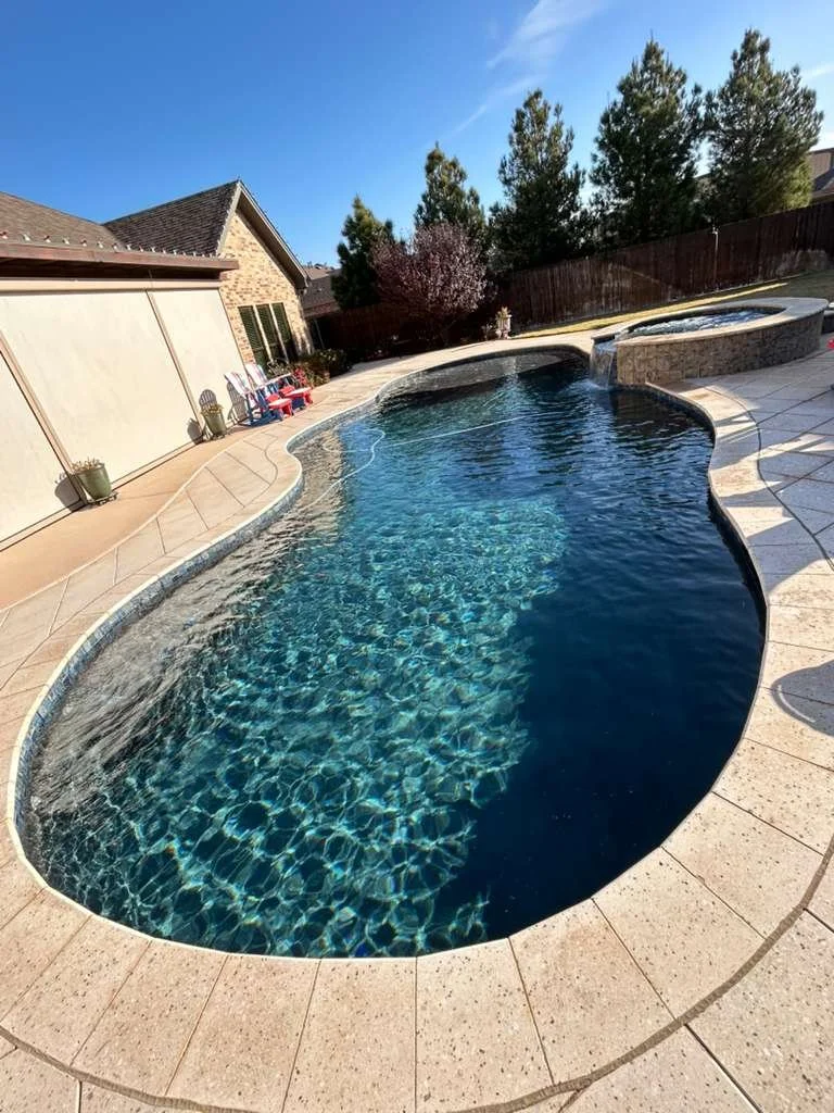 Freeform backyard pool with stone spa and deep blue water finish.