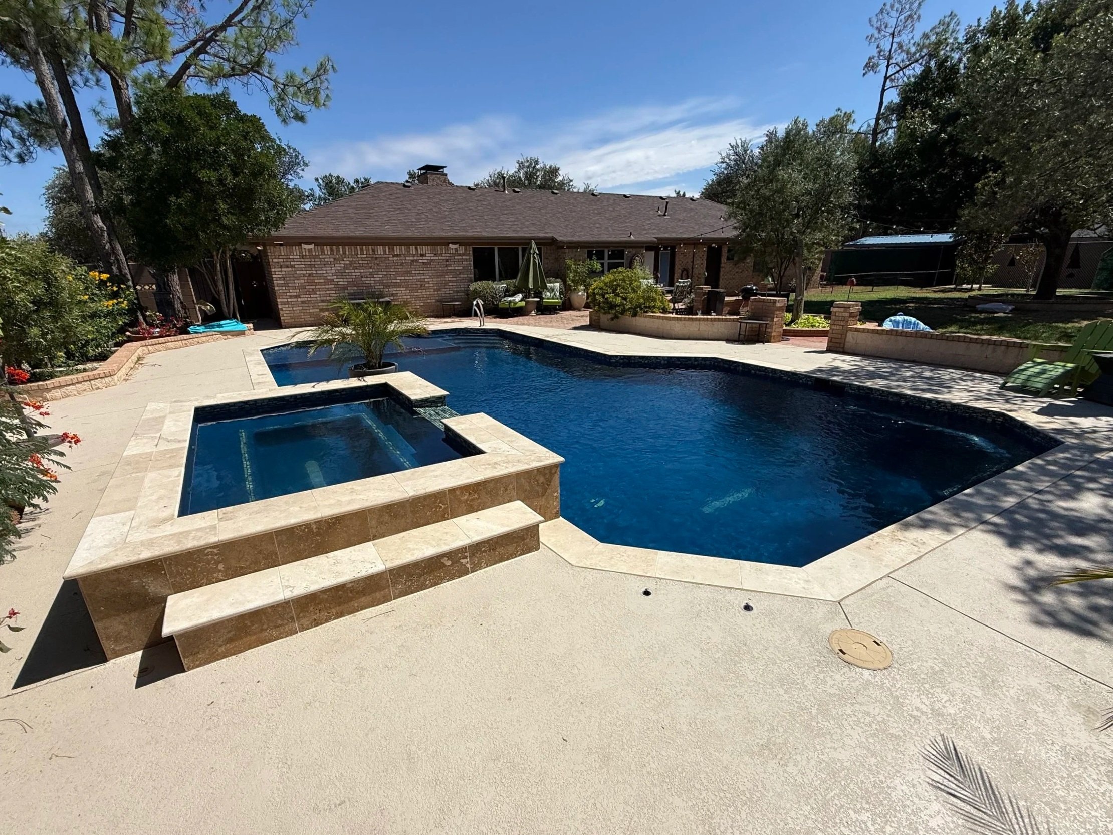 Clean residential pool with spa surrounded by landscaping and trees by Pool and Tech services by Emmanuel.