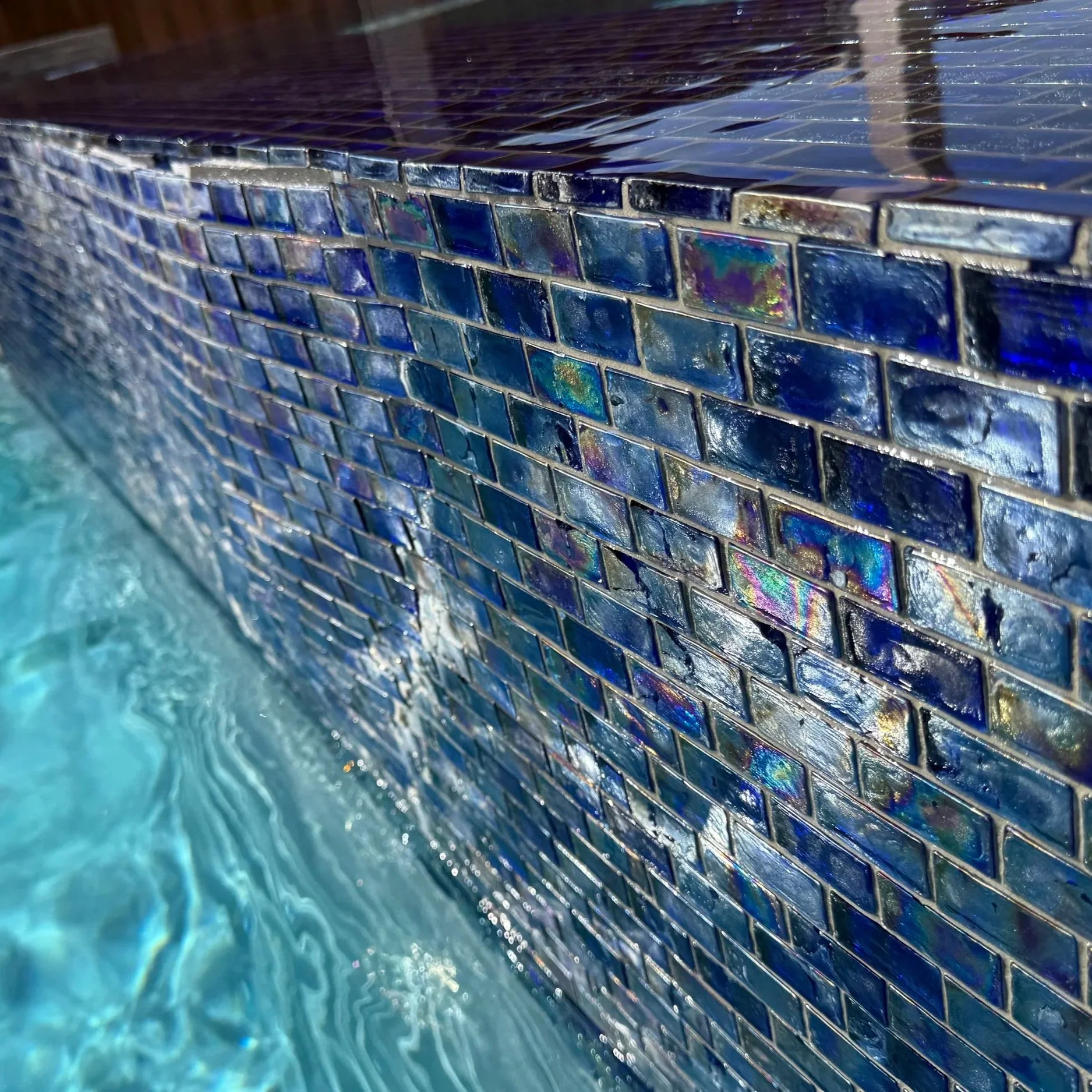 Close-up view of blue mosaic tile and flowing water at a commercial pool, showcasing professional maintenance for commercial pool systems in Midland, Texas.