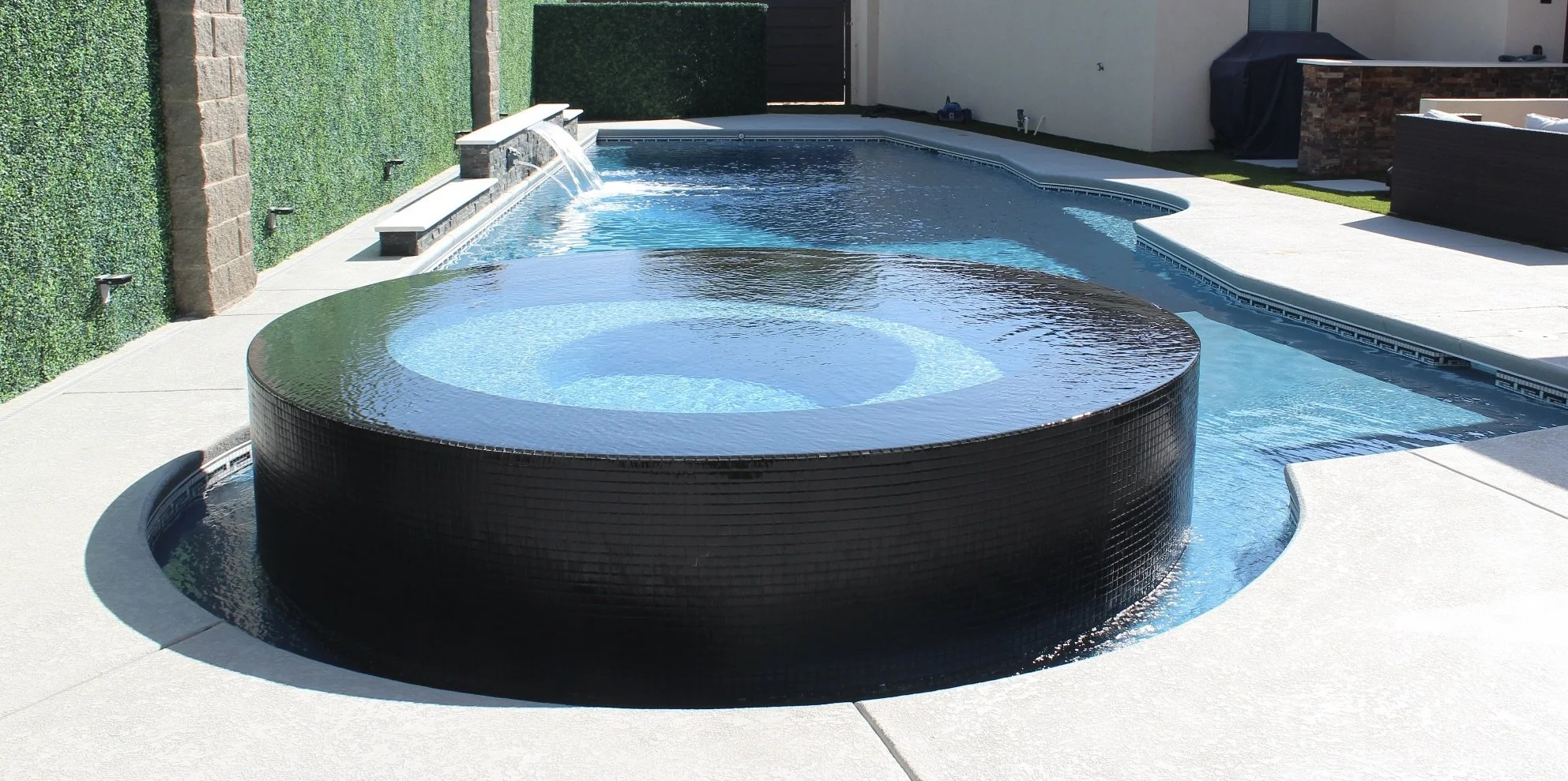 Modern circular spa overflowing into pool with water features.