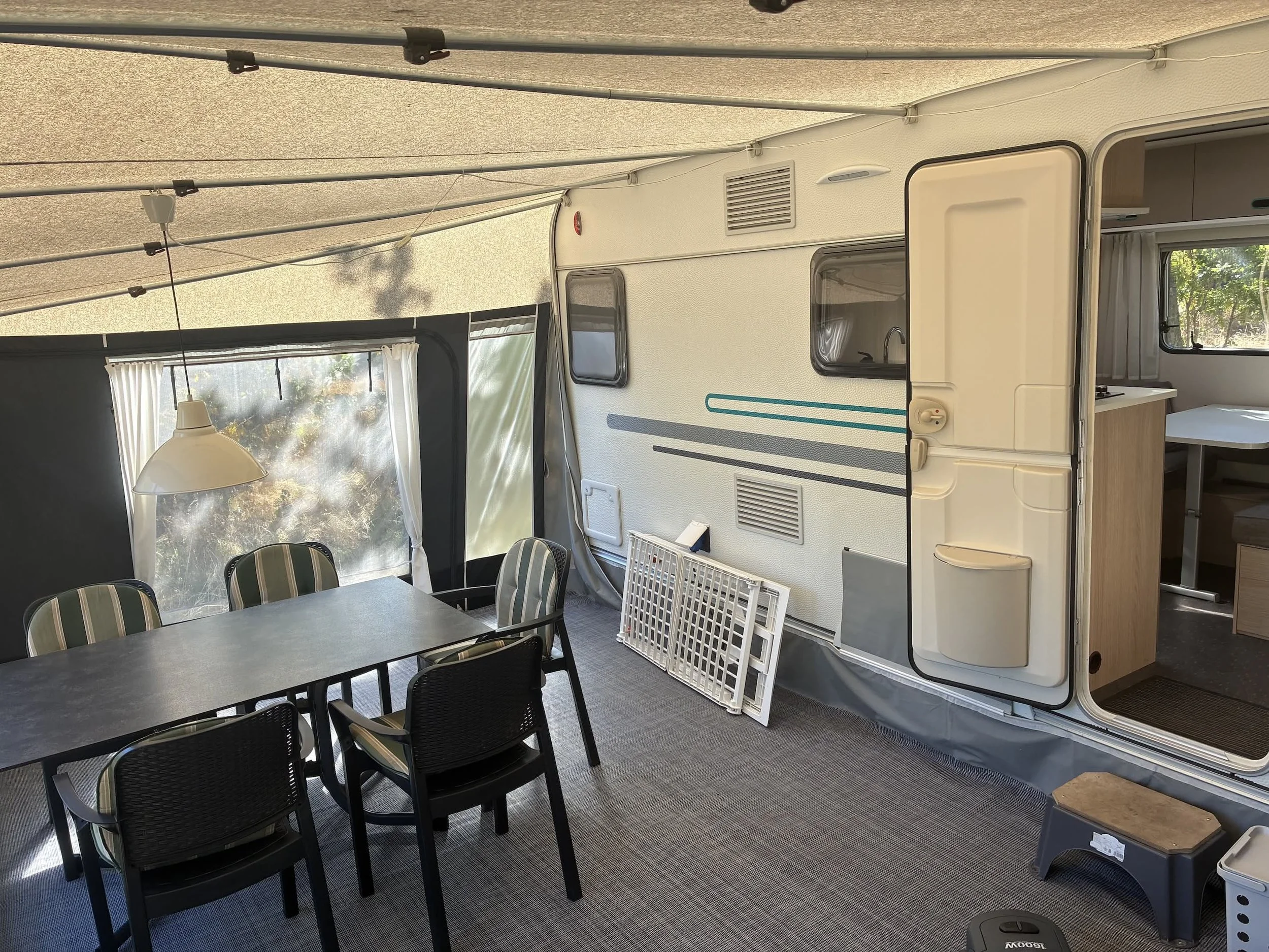 Indendørs billede af en campingvogns stue med spisestue, bord og stole, og åbent dør til køkkenet, med vindue, der giver udsigt til natur.