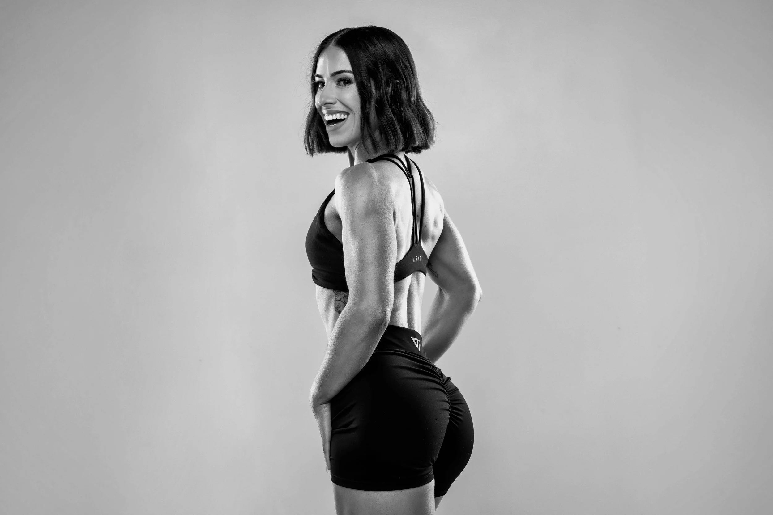 A woman with short dark hair smiling and looking at the camera, in athletic attire, posing against a plain background.