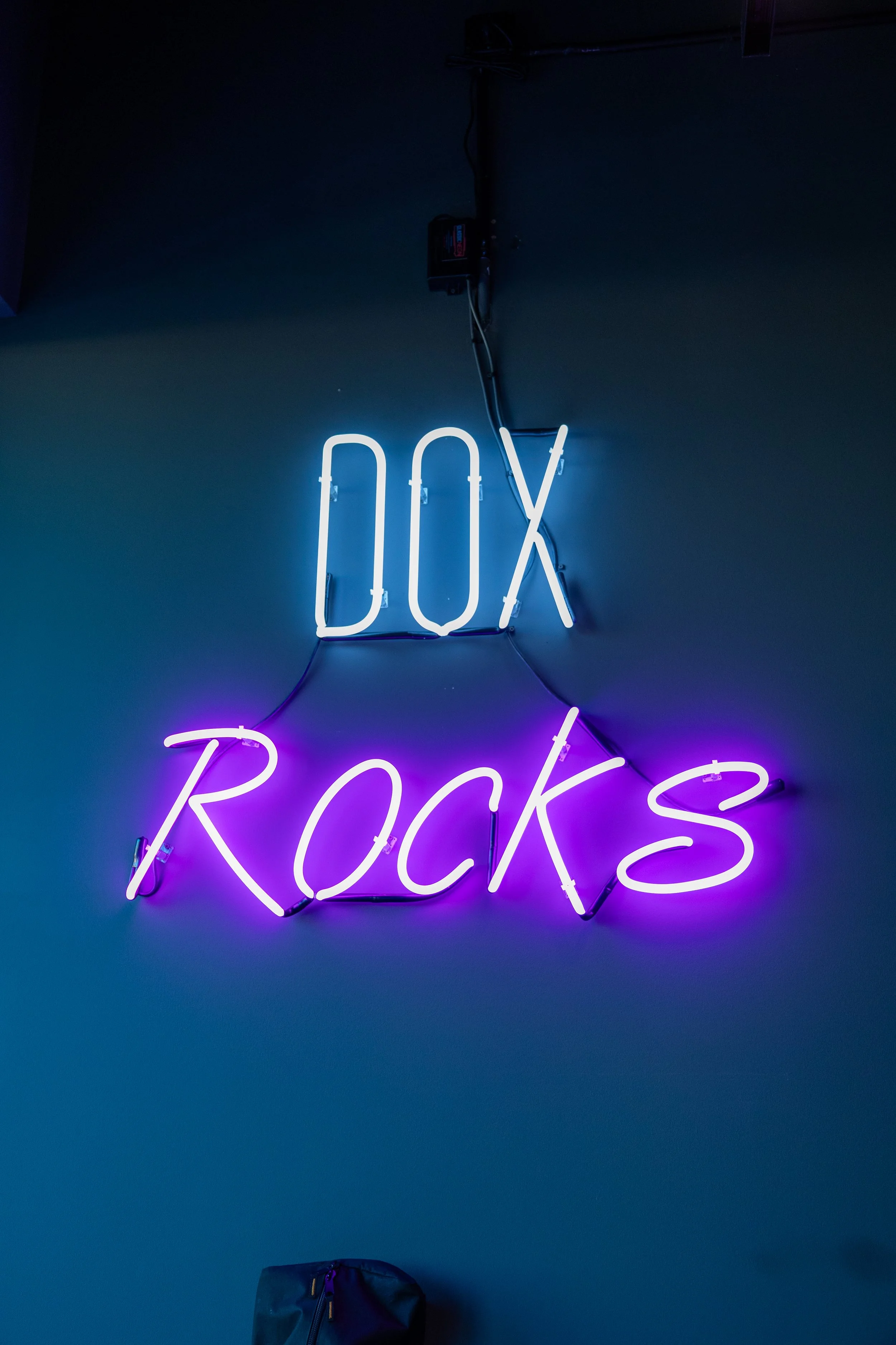 Neon sign on a wall that reads 'DOX ROCKS' with 'DOX' in white and 'ROCKS' in purple.