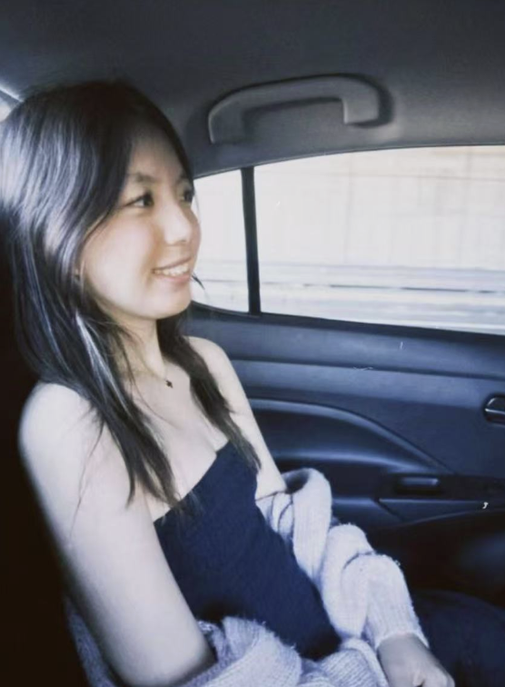 A young woman sitting in the backseat of a car, smiling and looking out the window.