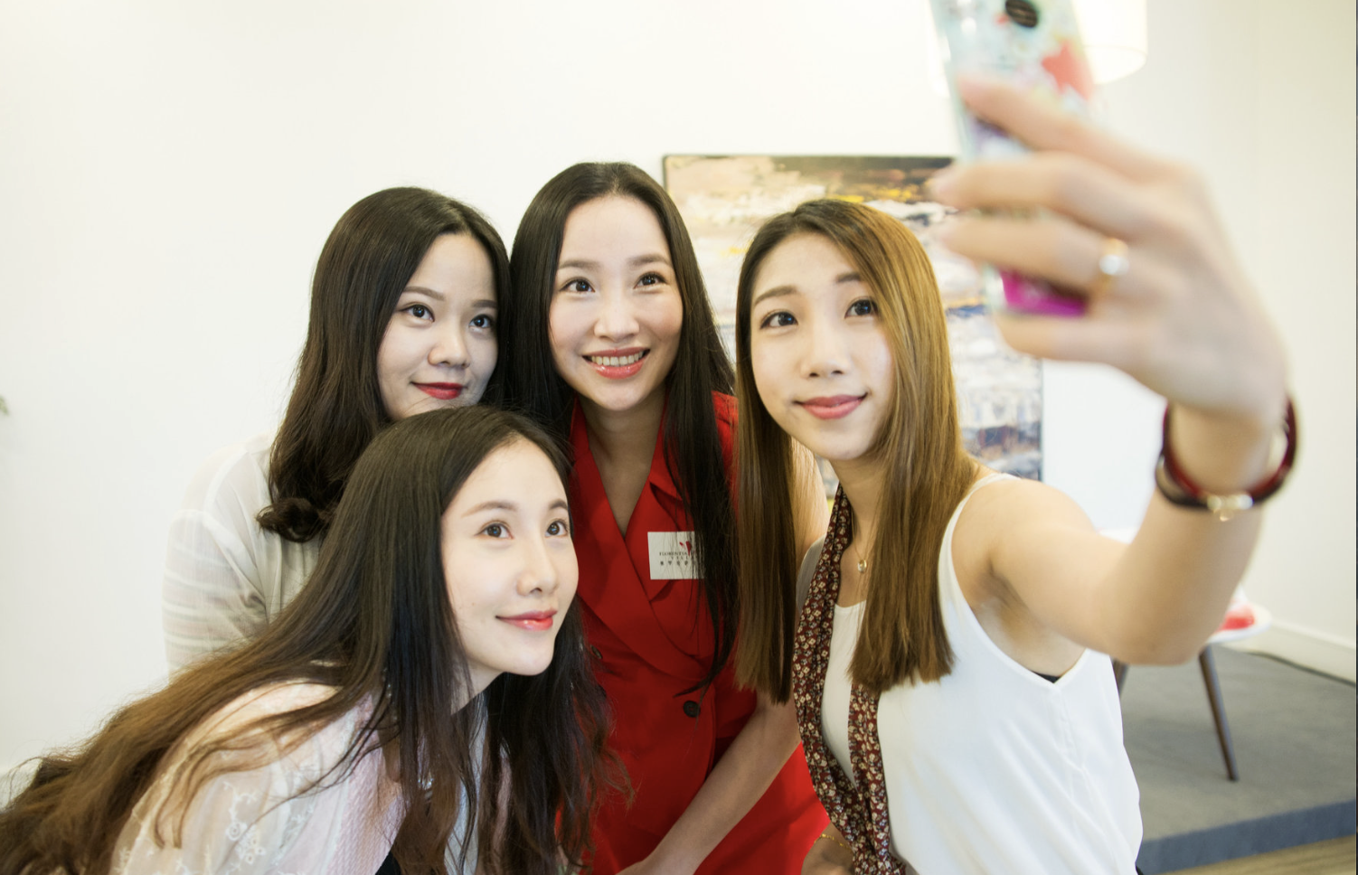 Four women taking a selfie together in a well-lit room with artwork on the wall.