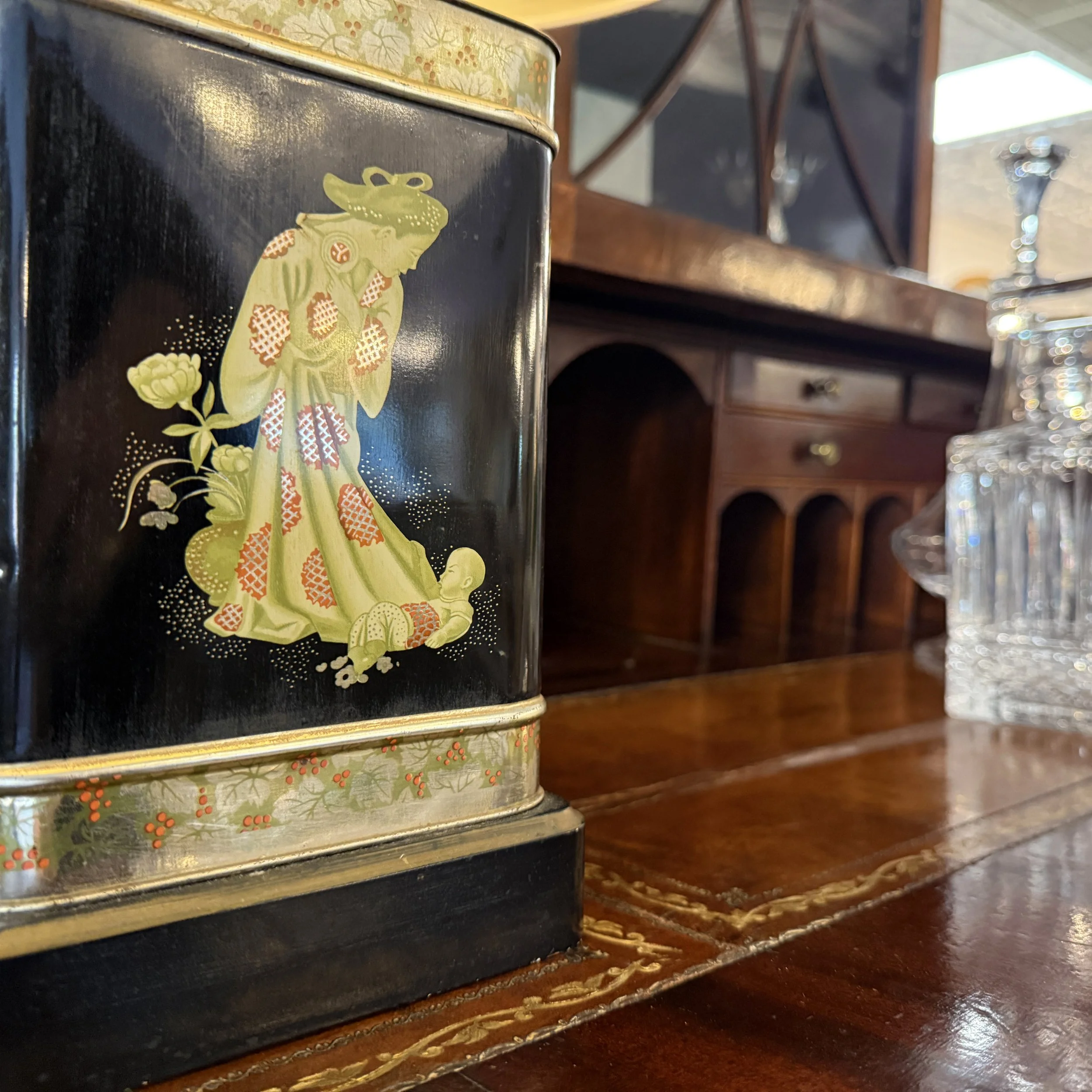 Close-up of a decorative vintage tin featuring an illustration of a woman in traditional clothing holding a child, placed on a wooden table.