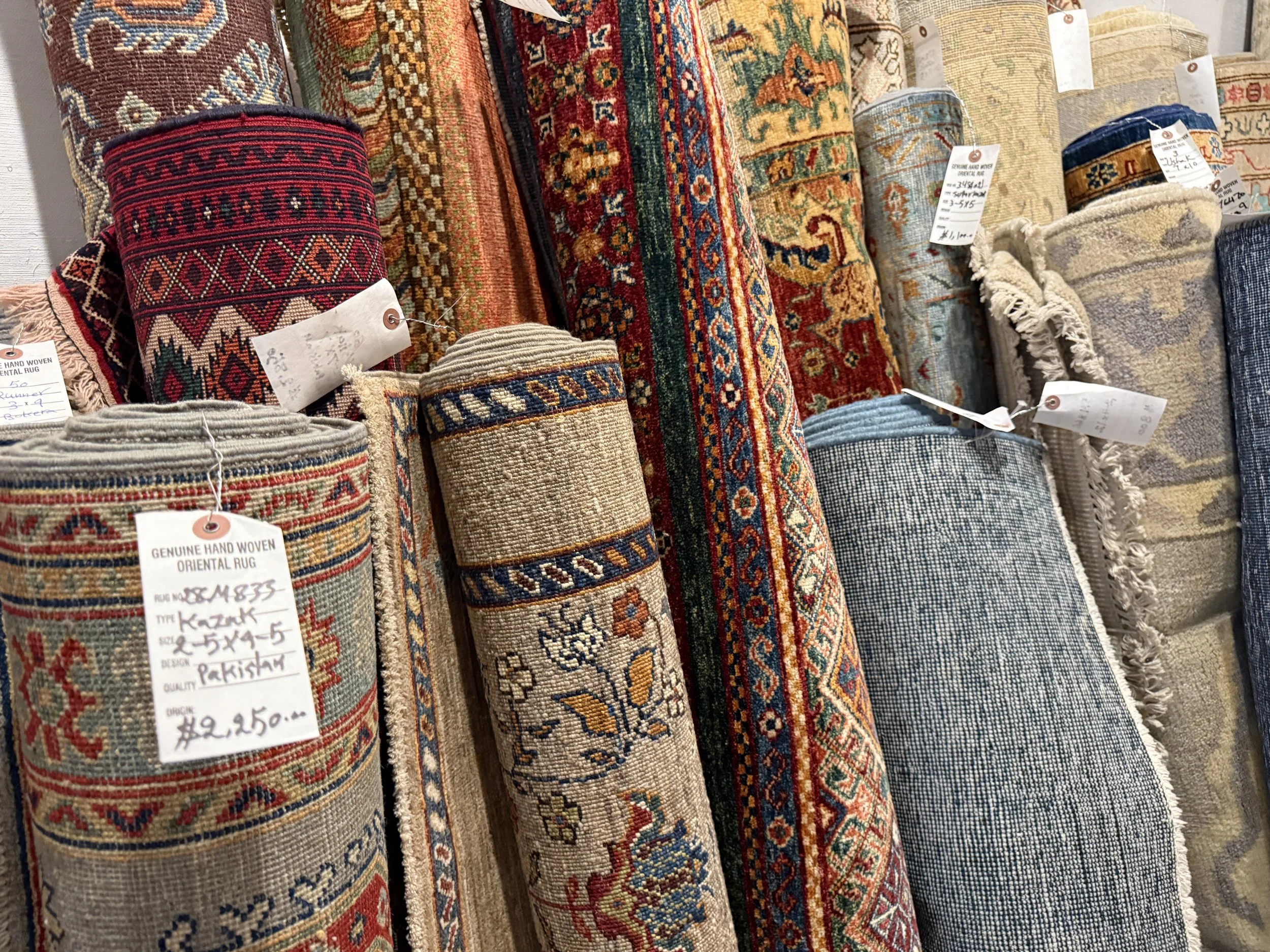 Stacked handwoven rugs with intricate patterns, including geometric and floral designs, displayed at a store.