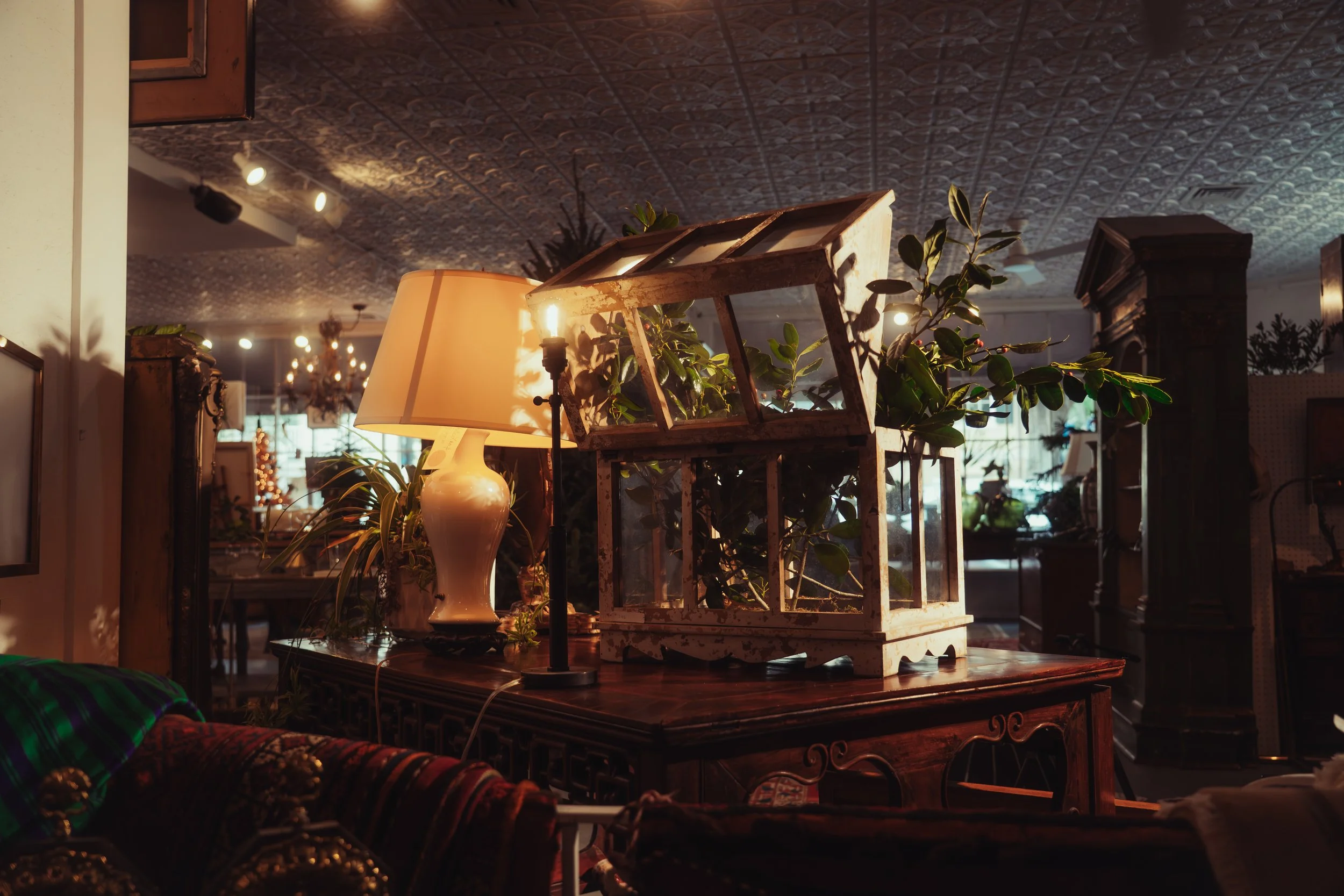A vintage wooden table with two drawers and curved legs, placed against a plain white wall. On top of the table is a decorative bowl filled with smooth, rounded stones of various colors.