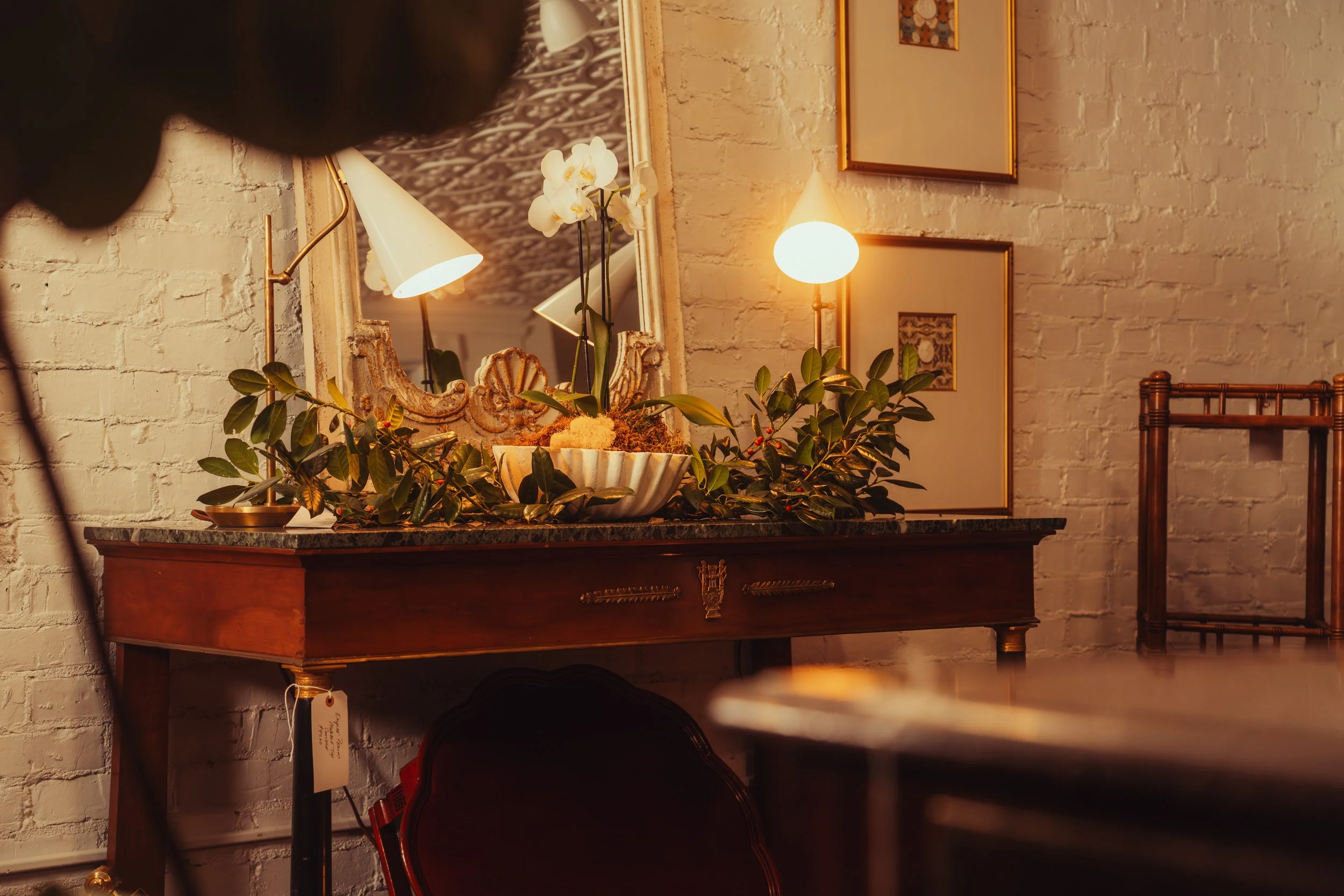 Living room corner with wall art, a wooden console table, a mirror, a table lamp, a plant, and a cream-colored sofa and chair with pillows.