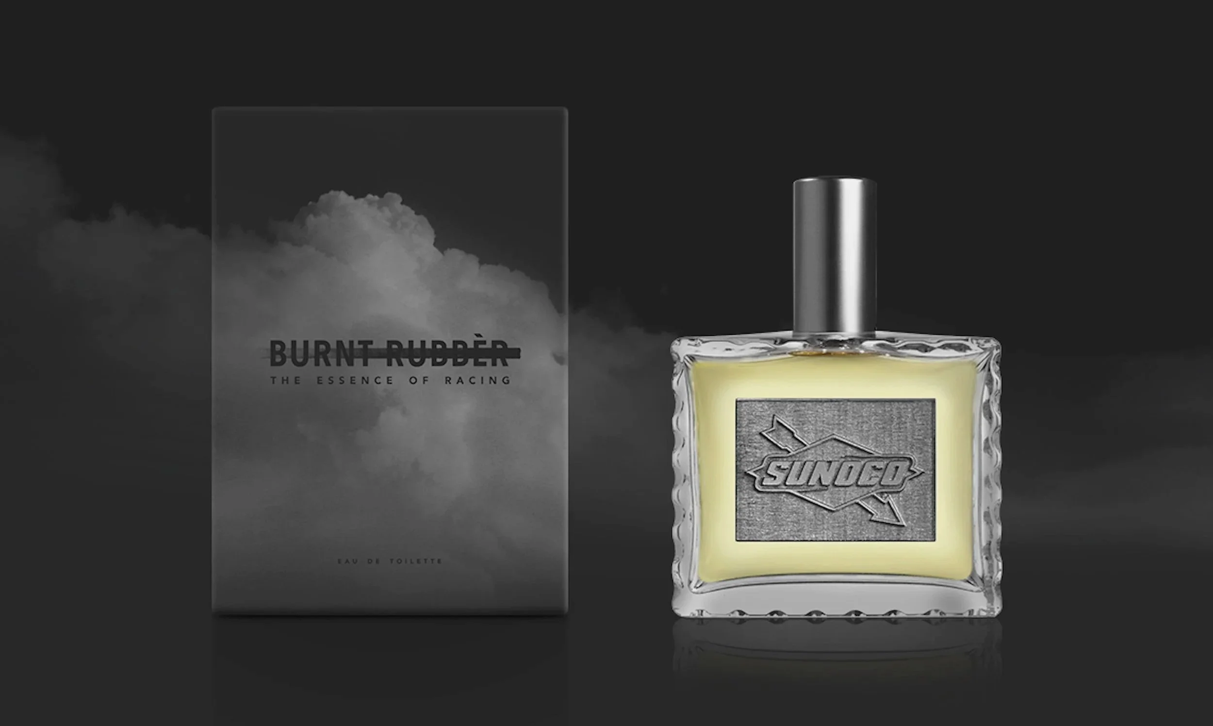 A bottle of Sunoco-branded scent next to its packaging with the label \"Burnt Rubber\" and the tagline \"The Essence of Racing,\" set against a dark background with subtle reflections.