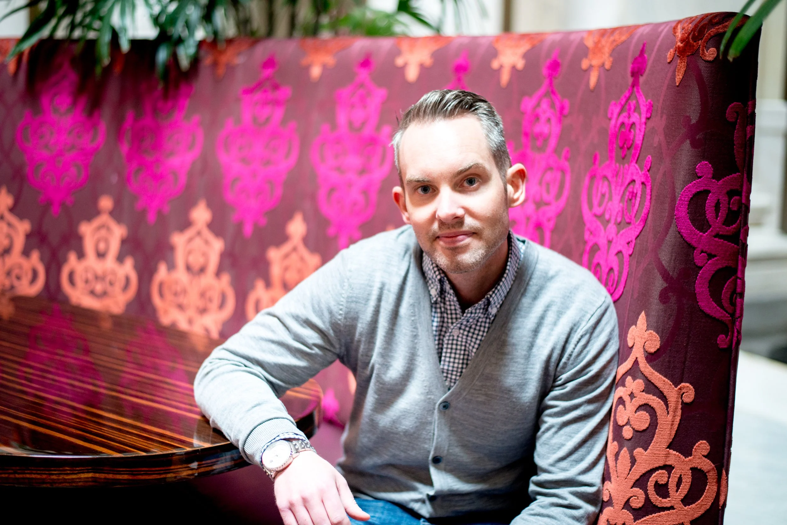 Wick Vipond sitting at a table with a decorative pink and orange patterned background.