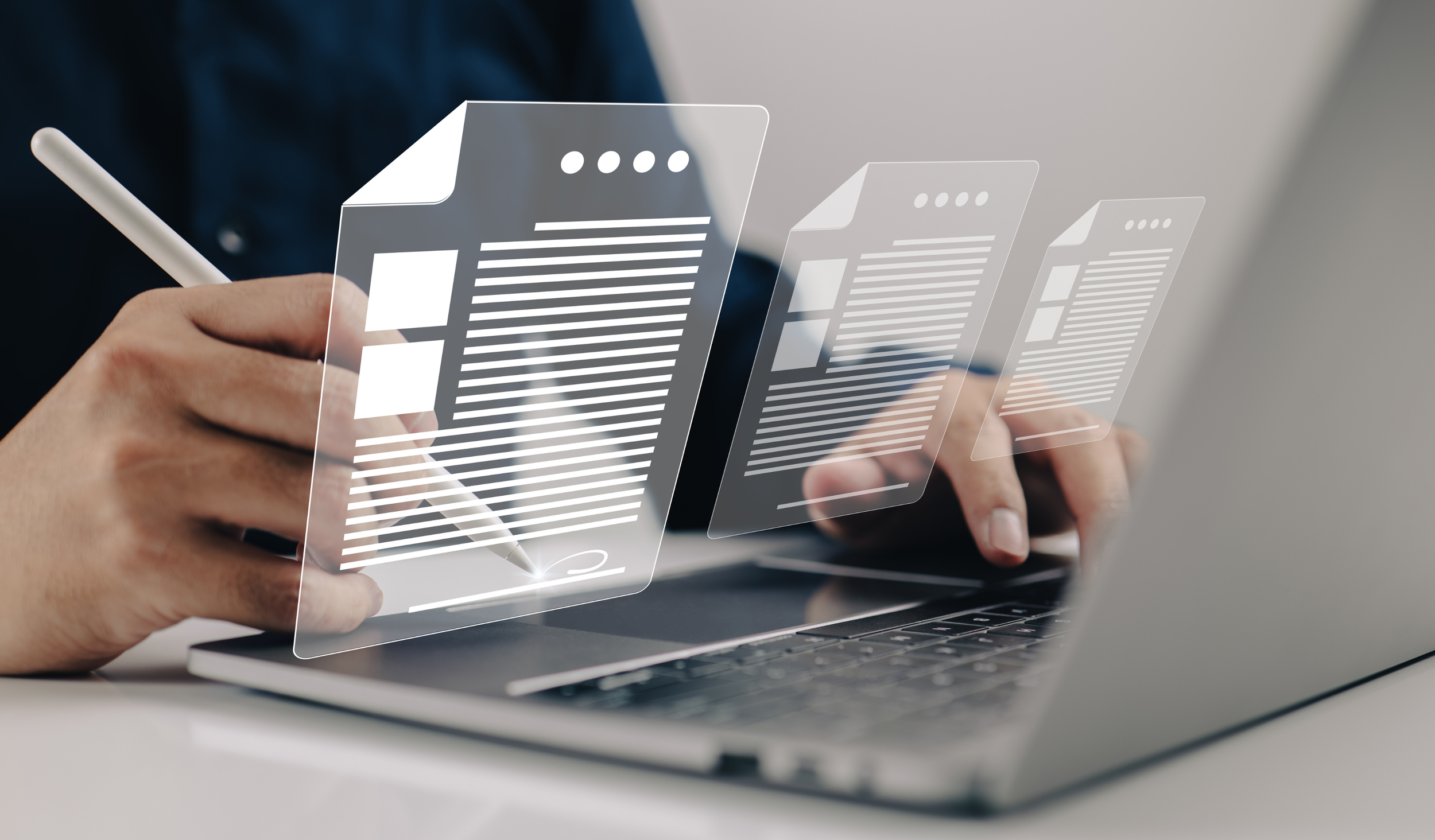 Person using a stylus on digital holographic screens with document icons over a laptop.