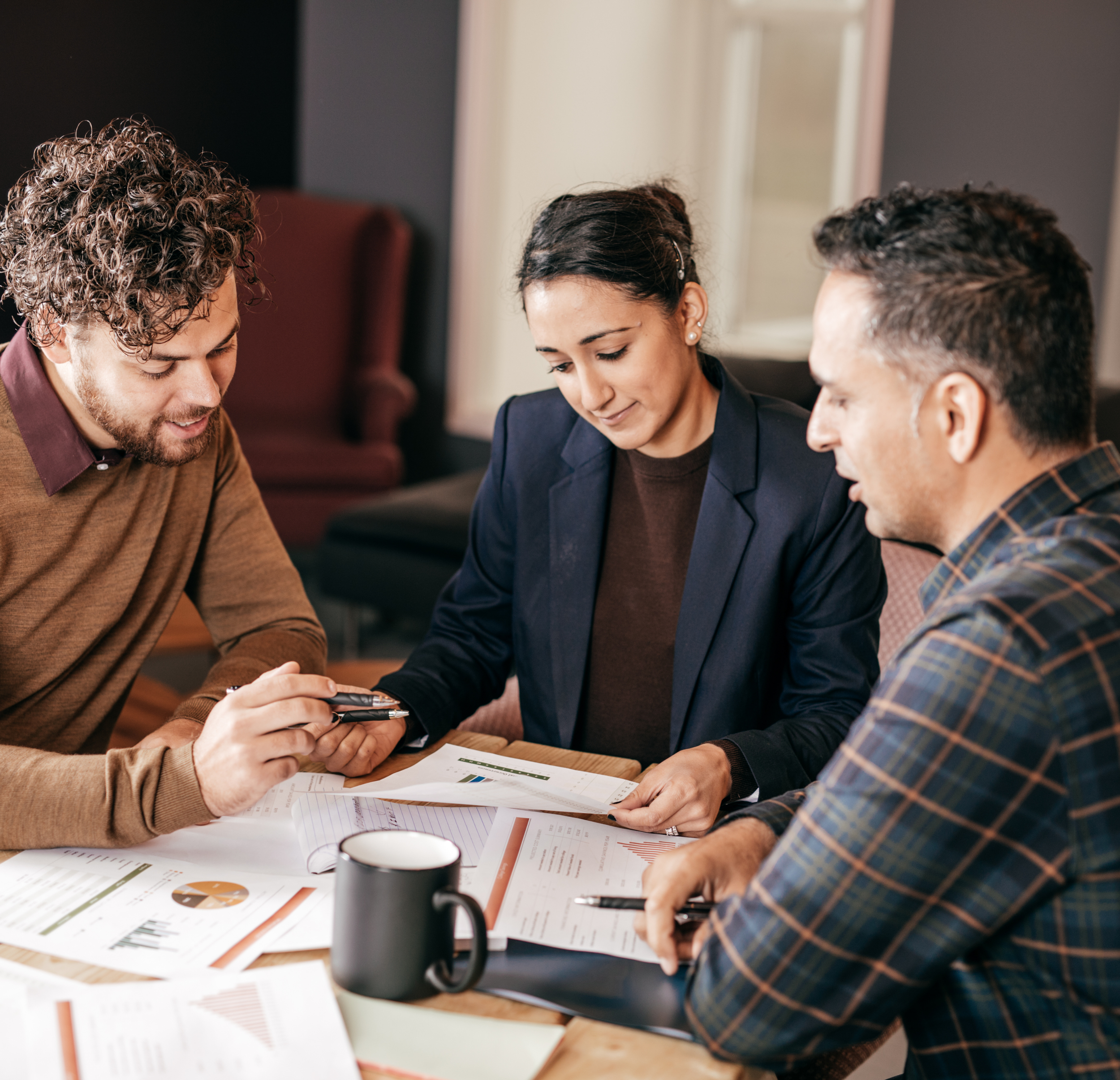 Three colleagues reviewing documents and charts during a meeting in an office conference room.