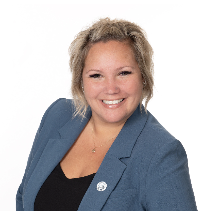 A woman with blonde hair styled in loose waves, wearing a blue blazer over a black top, smiling at the camera against a plain white background.