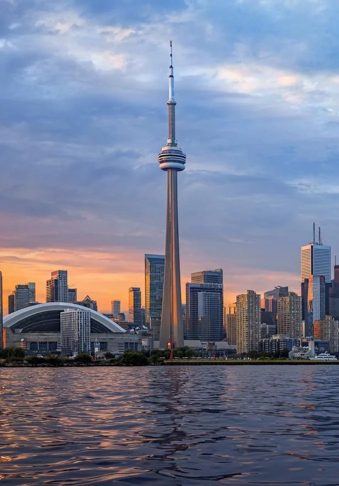 Toronto skyline with the CN Tower at sunset, reflected in a body of water in the foreground.