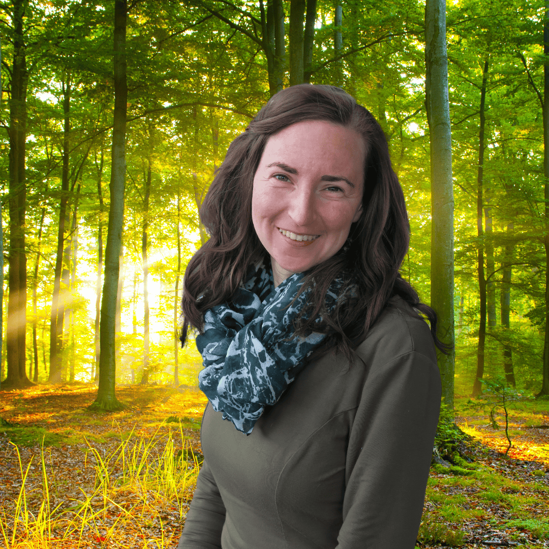 Lächelnde Frau vor einem Sonnenaufgang im Wald mit grünen Blättern und Sonnenstrahlen.