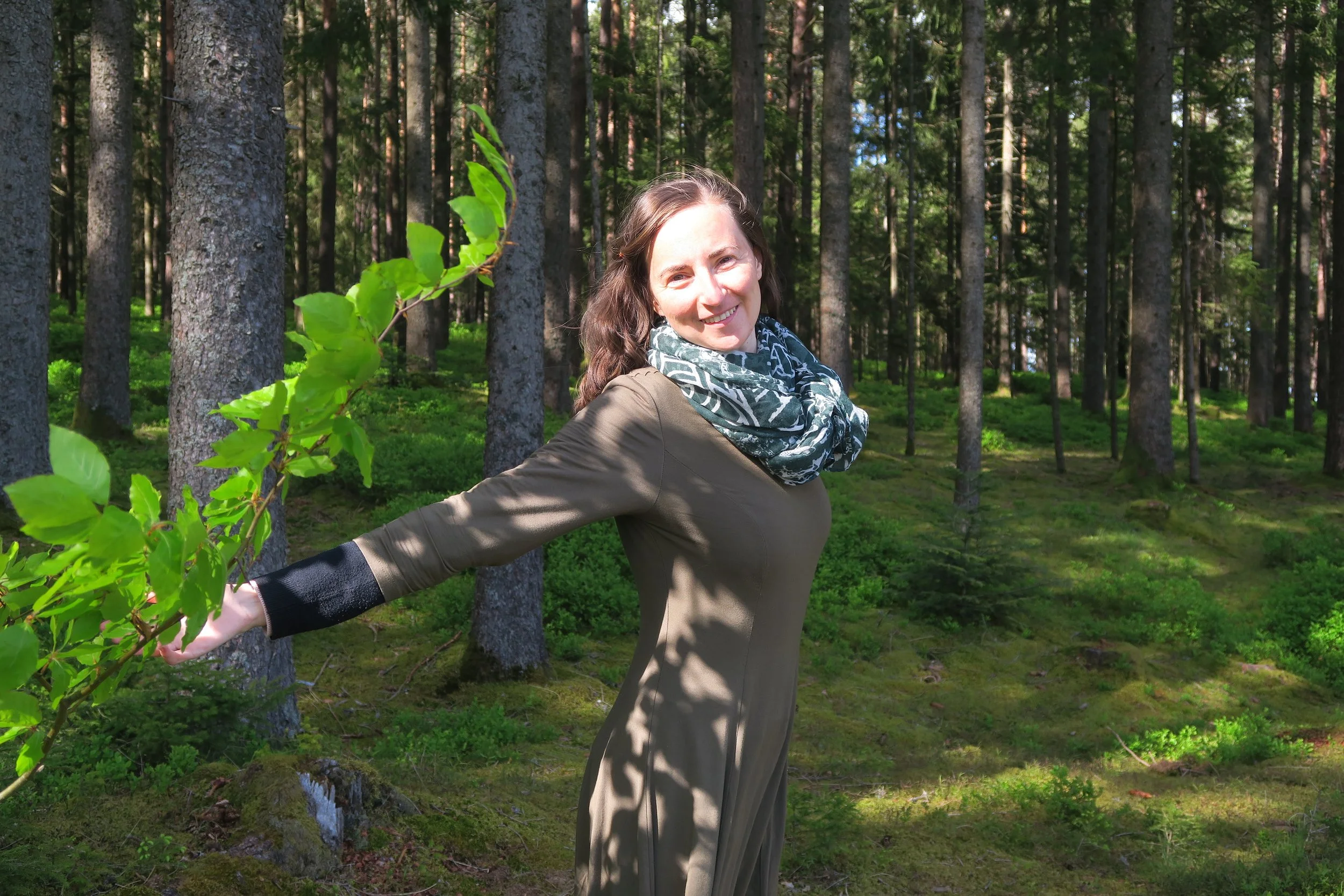 Eine lachende Frau im Wald, die mit einem Ast nach hinten greift.