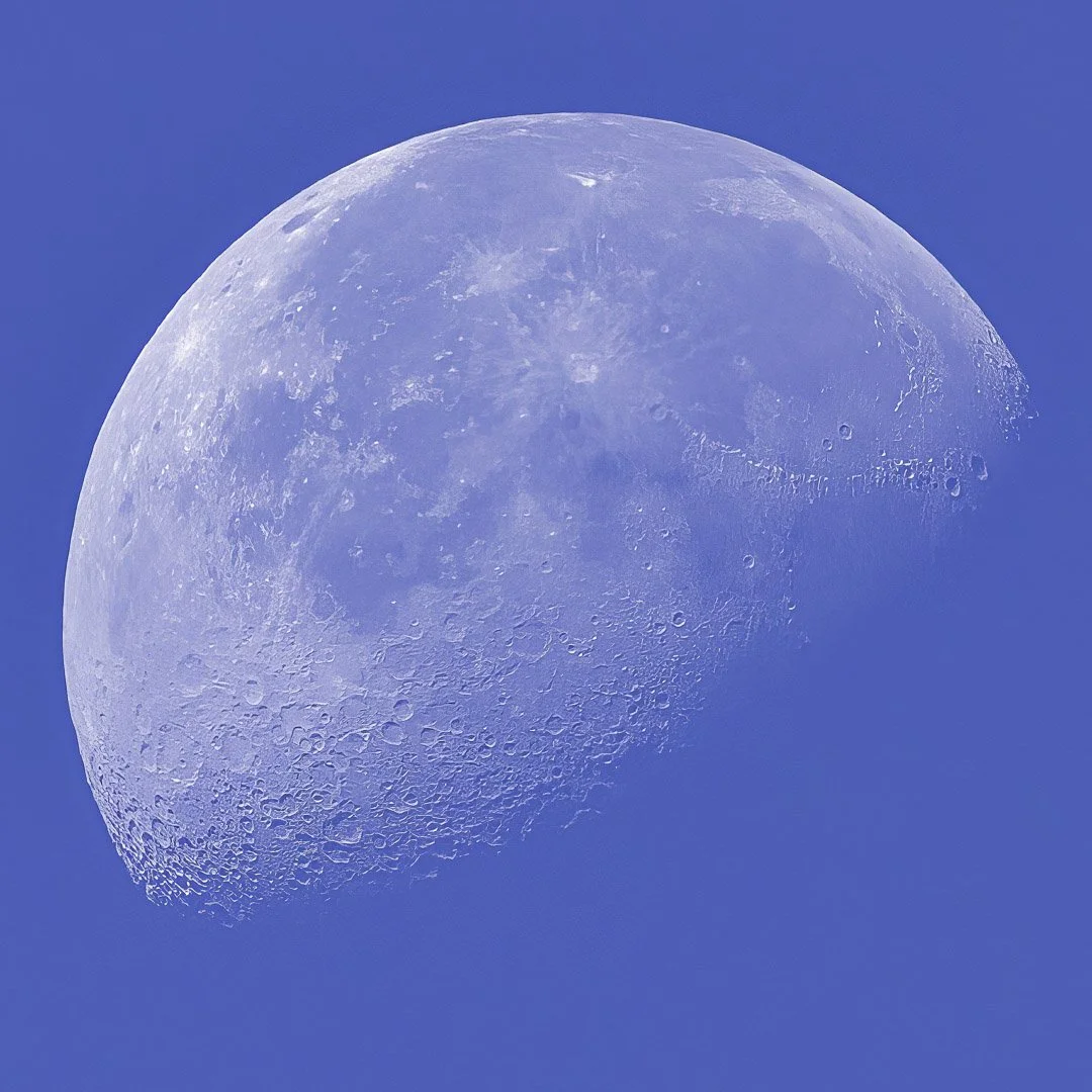 Detailed view of the Moon photographed against a clear blue daytime sky.