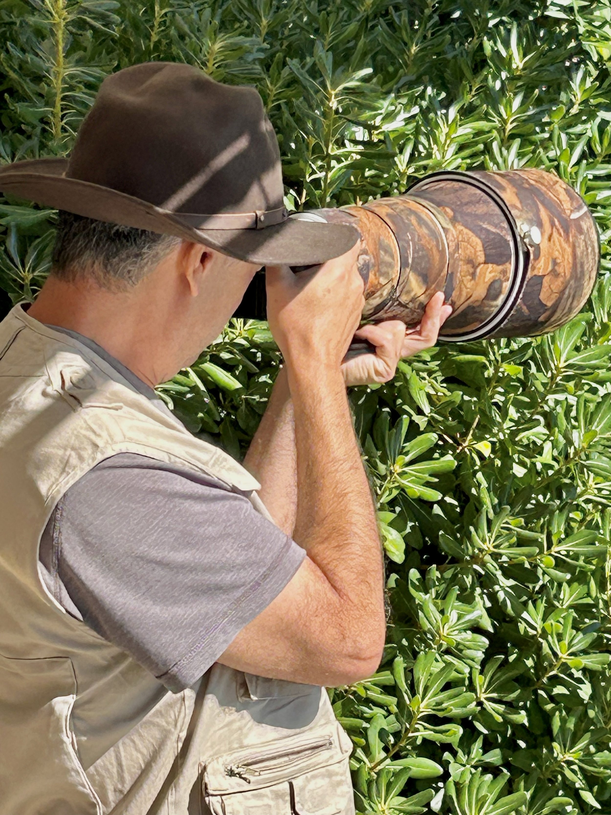 Joseph shooting with a 400mm telephoto lens from inside thick vegetation during a wildlife session.