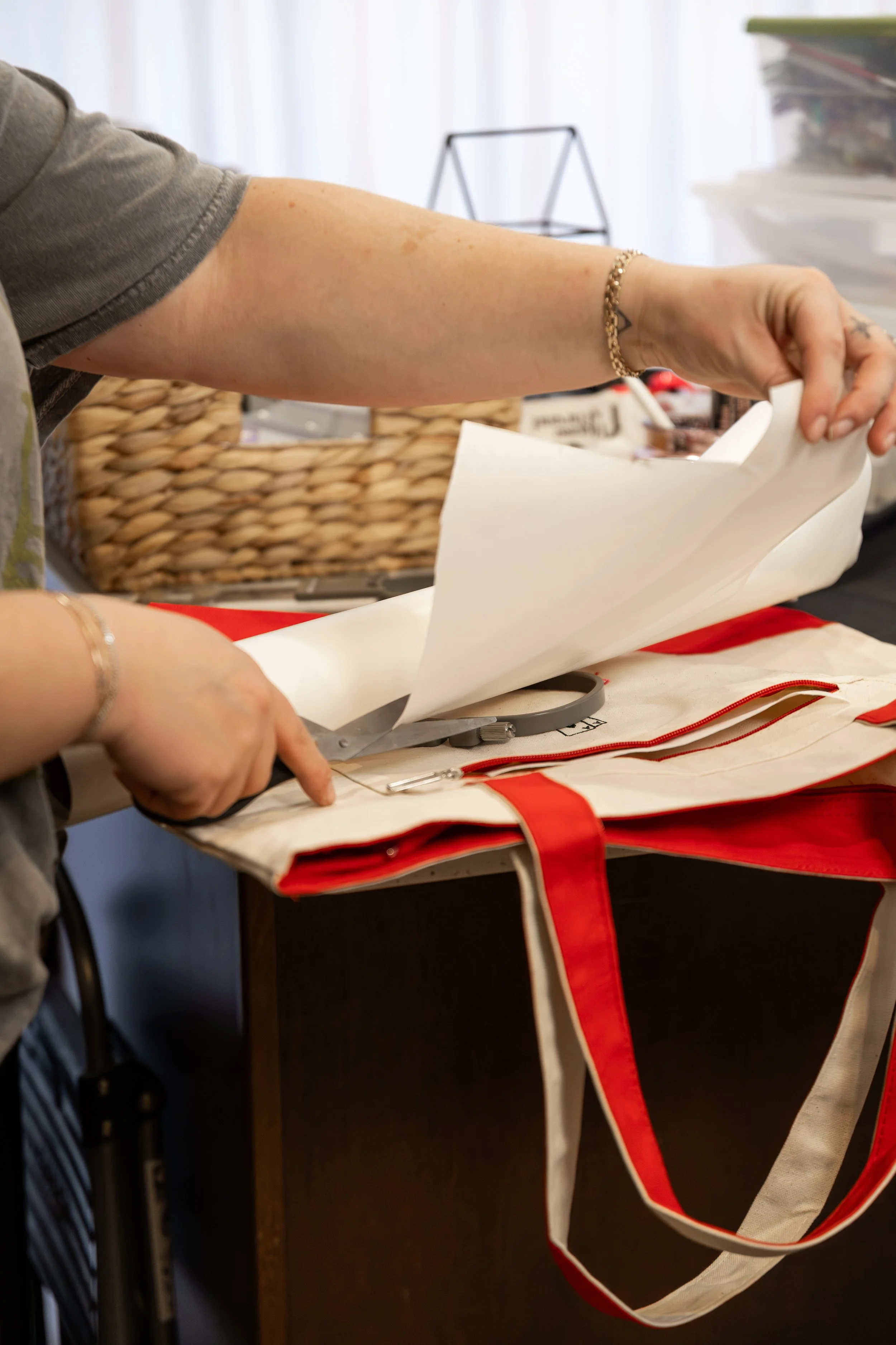 Person cutting a piece of fabric with scissors on a worktable, surrounded by sewing supplies.