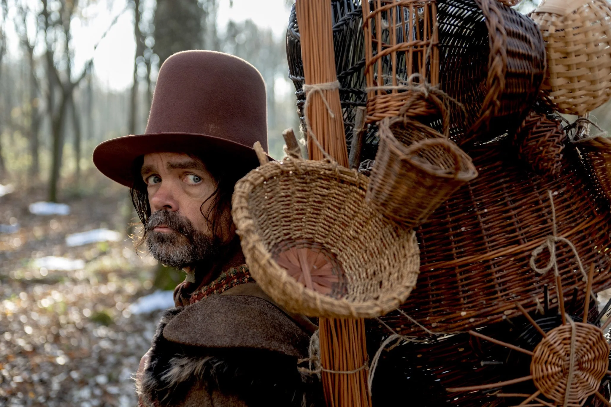 In Alex Huston Fischer and Eleanor Wilson's film WICKER (2026), The Basketmaker (Peter Dinklage) looks over his shoulder by the pile of baskets he carries through the woods.