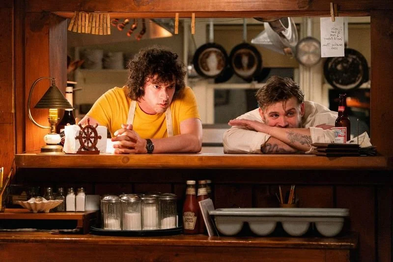 In Matt Johnson's biopic about Anthony Bourdain, TONY, Tony (Dominic Sessa) and Sal (Leo Woodall) lean through the order passthrough window of crab shack The Flagship's kitchen in Cape Cod.