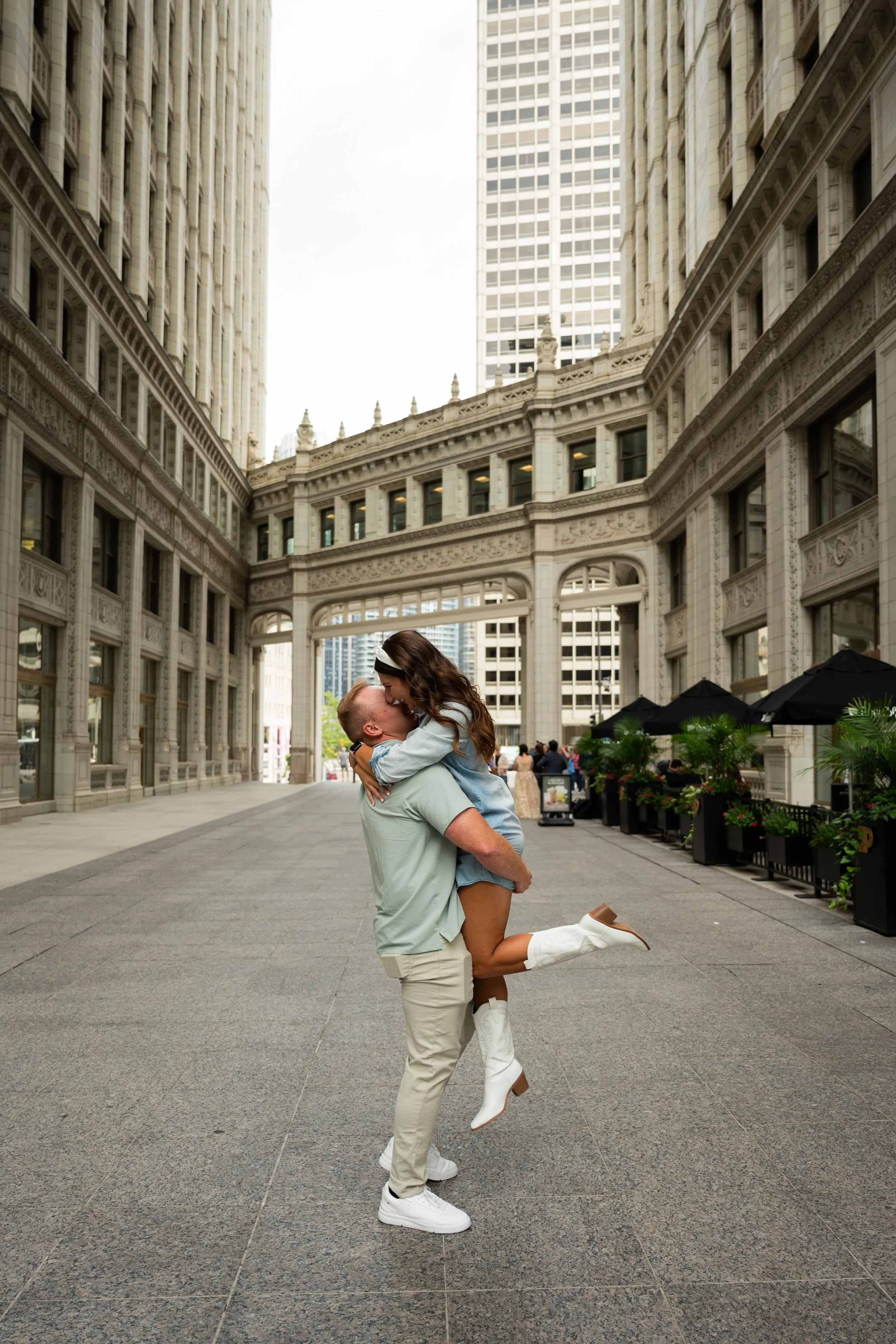 A man kneeling and lifting a woman in an embrace on a city street with historic and modern buildings in the background.