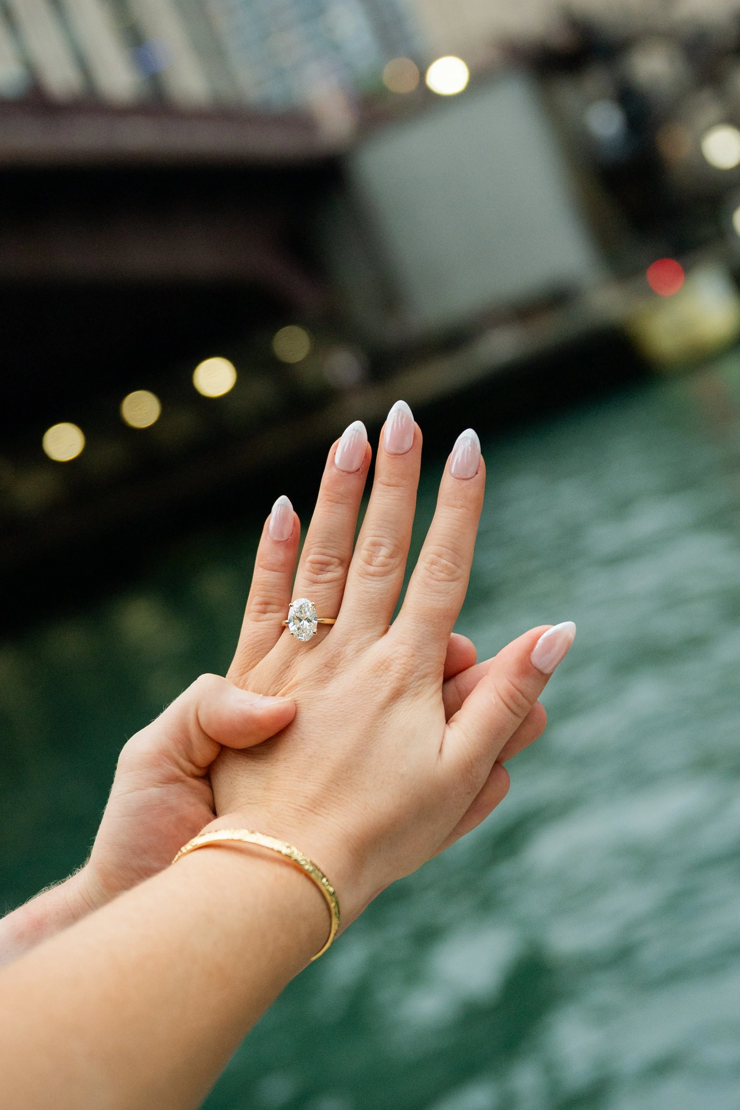Close-up of two hands with wedding rings and bracelets, one person's hand resting on another’s, against a blurred background.