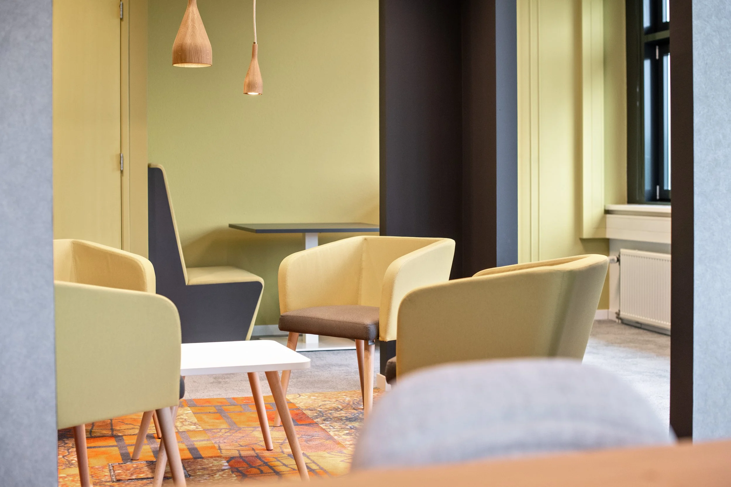 Een moderne eetkamer met gele stoelen en een muur met groene en donkere tinten, hanglampen en een raam.