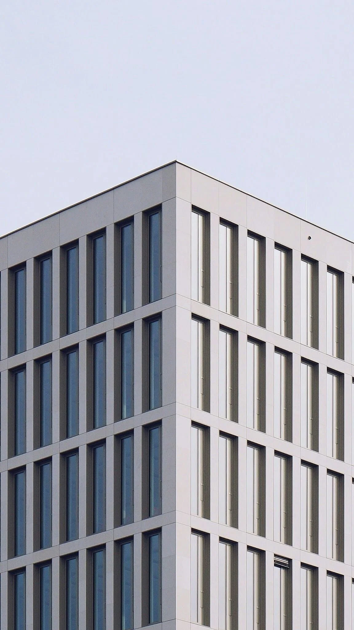 Modern kantoorgebouw met grote ramen en een grijze gevel, zichtbaar tegen een heldere, lichte hemel.