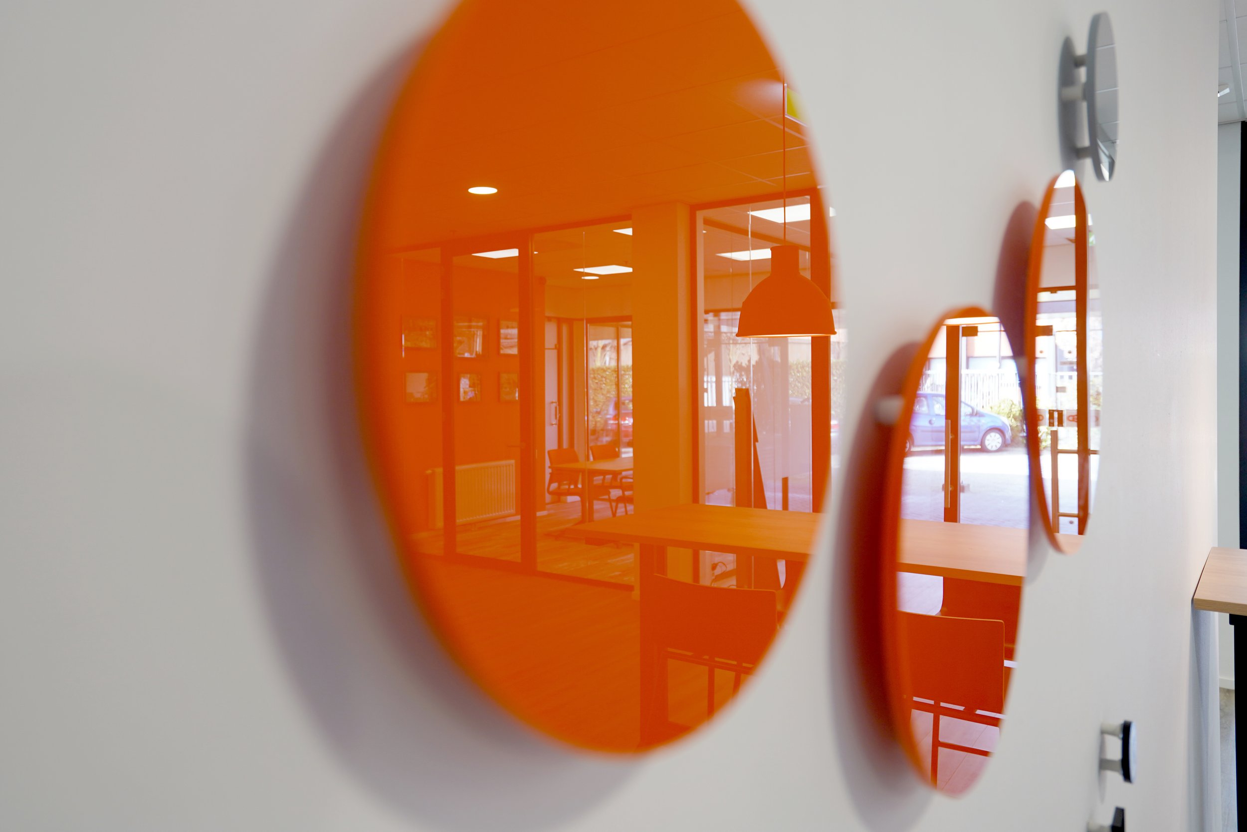 Binnenkant van een modern gebouw met grote ramen en oranje elementen, gezien door een oranje spiegel of raam.
